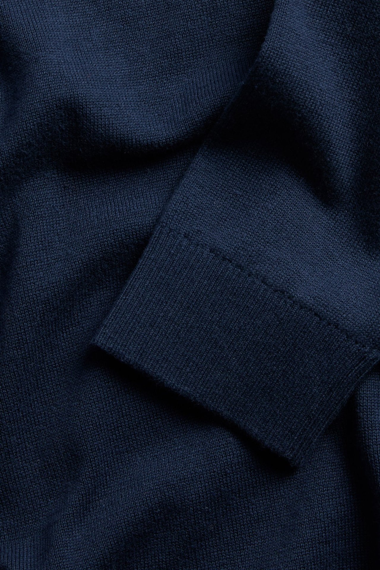Zbliżenie granatowego swetra z dzianiny z prążkowanym mankietem.