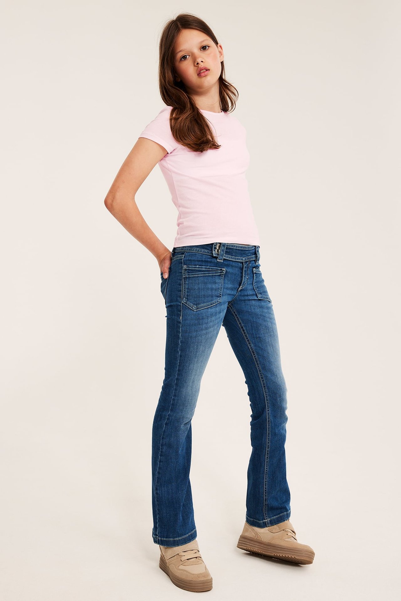 Frontvy av barn i blåa bootcut jeans, rosa t-shirt och beigefärgade platåskor.