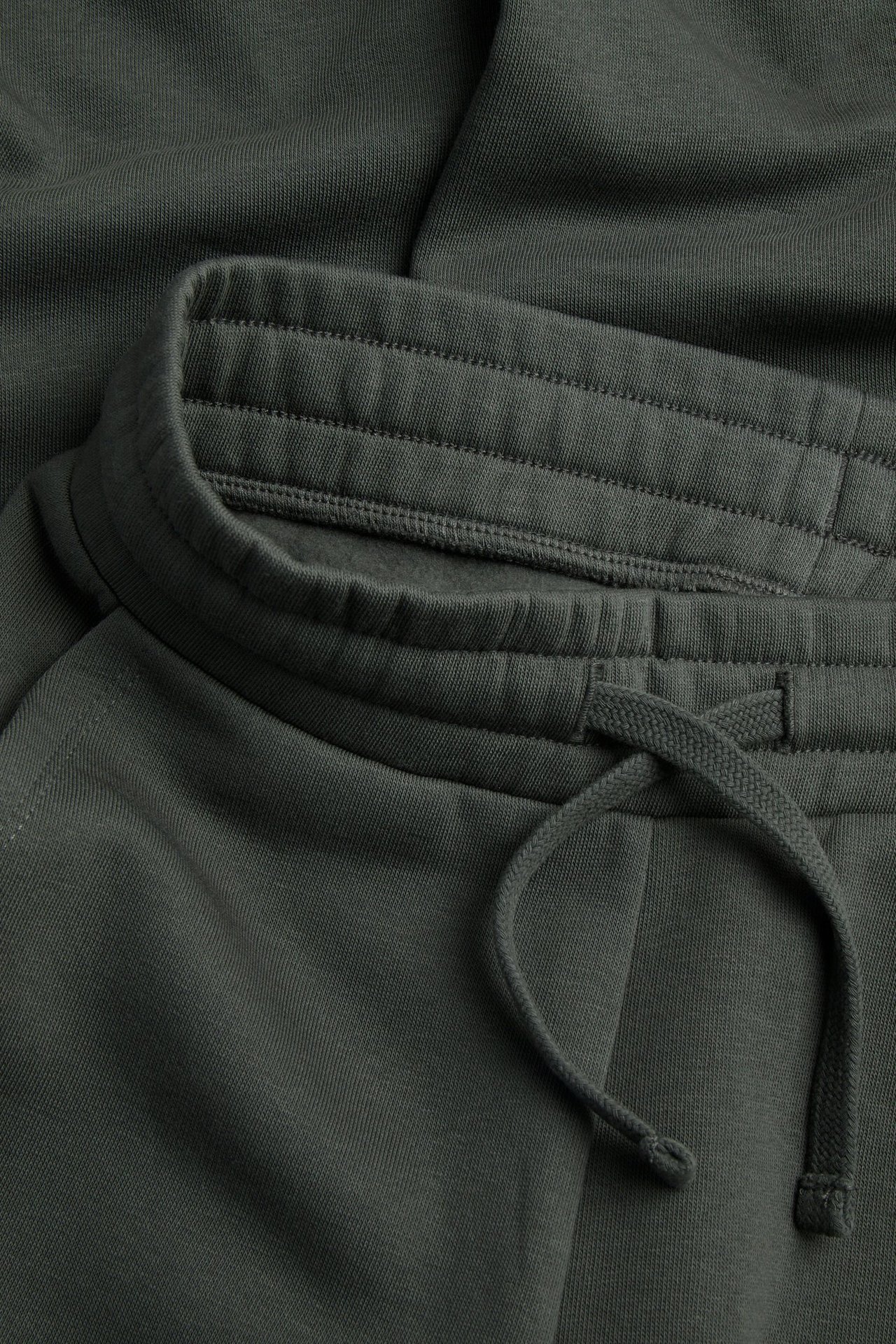 Lähikuva tummanvihreistä yksivärisistä puuvillasekoitehousuista, joustavalla vyötäröllä ja kiristysnyörillä.