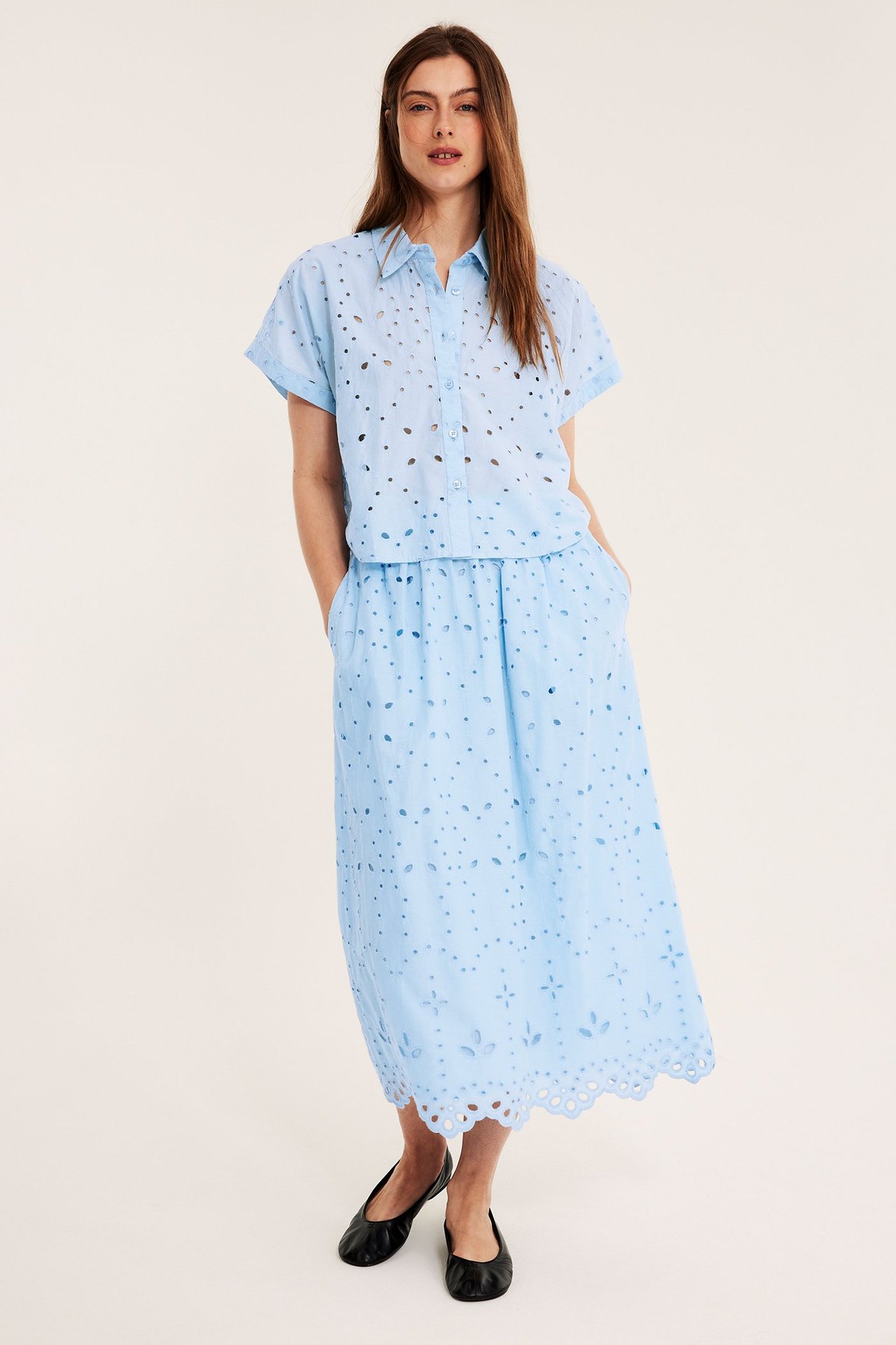 Edestä: Nainen vaaleansinisessä broderie anglaise -puserossa, midihameessa ja mustissa ballerinat.