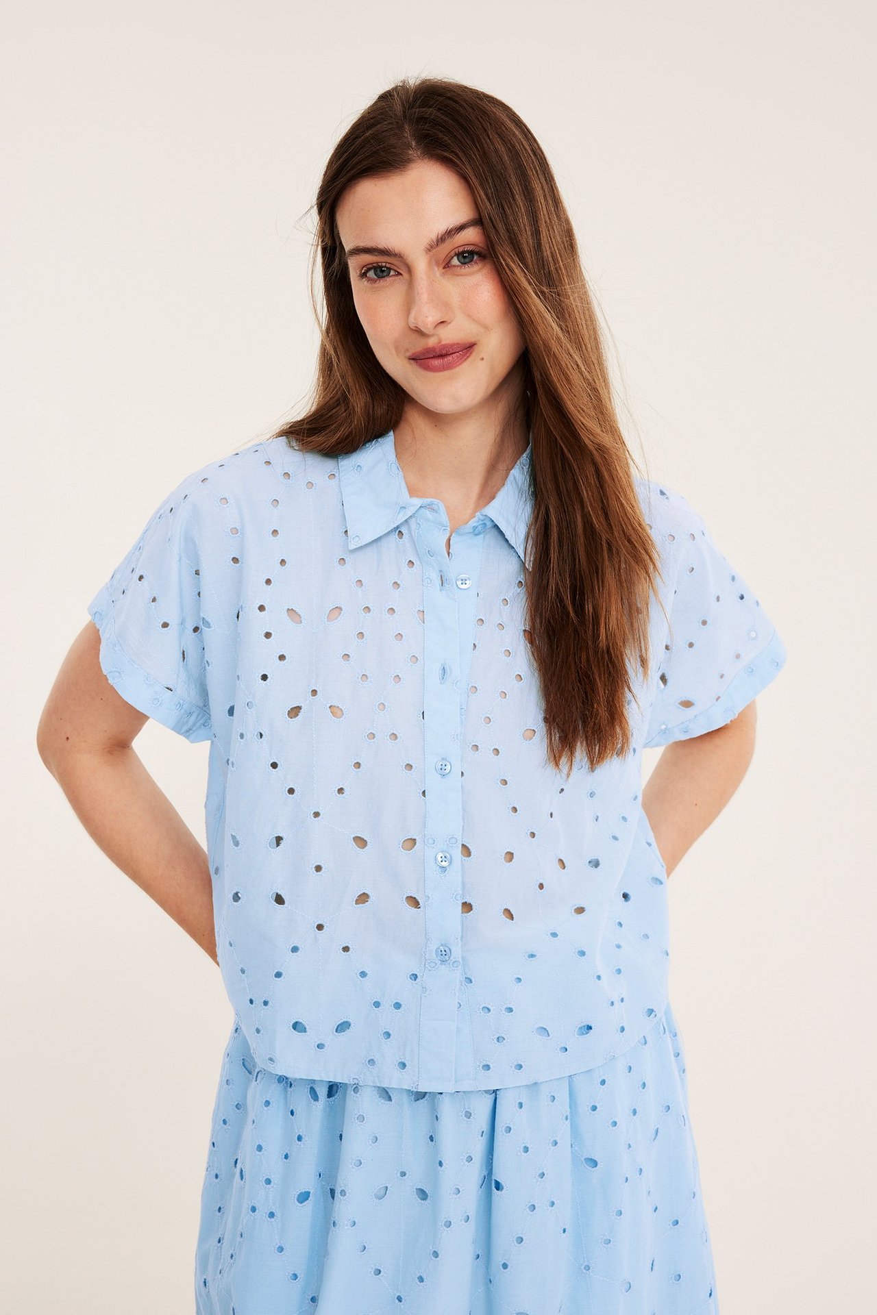 Edestä: Nainen yllään vaaleansininen puuvillainen broderie anglaise -lyhythihainen pusero, napit edessä ja yhteensopiva hame.