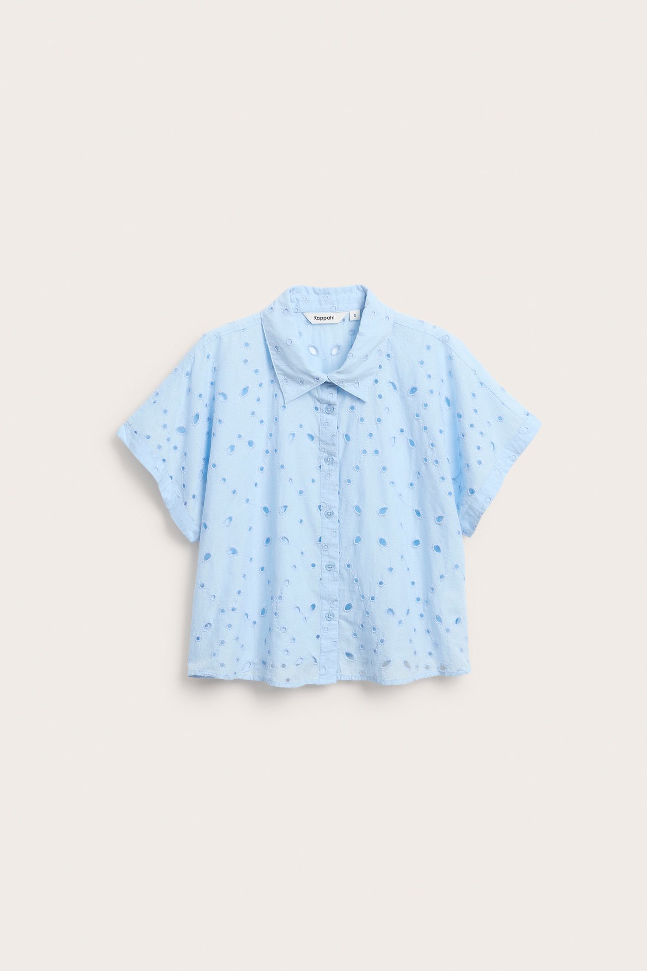 Frontvisning av en lyseblå kortermet bomullsbluse med broderie anglaise og knapper foran.