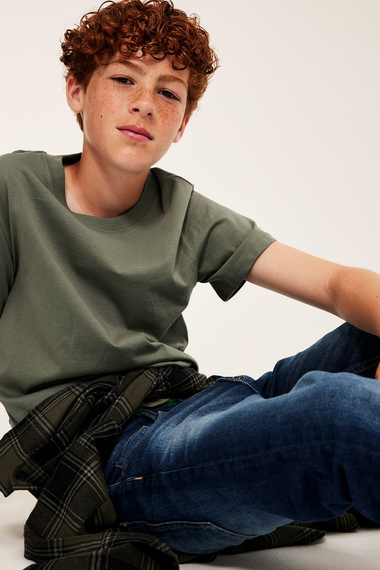 Framifrån av sittande barn i grön t-shirt, blå jeans och grönrutig skjorta.