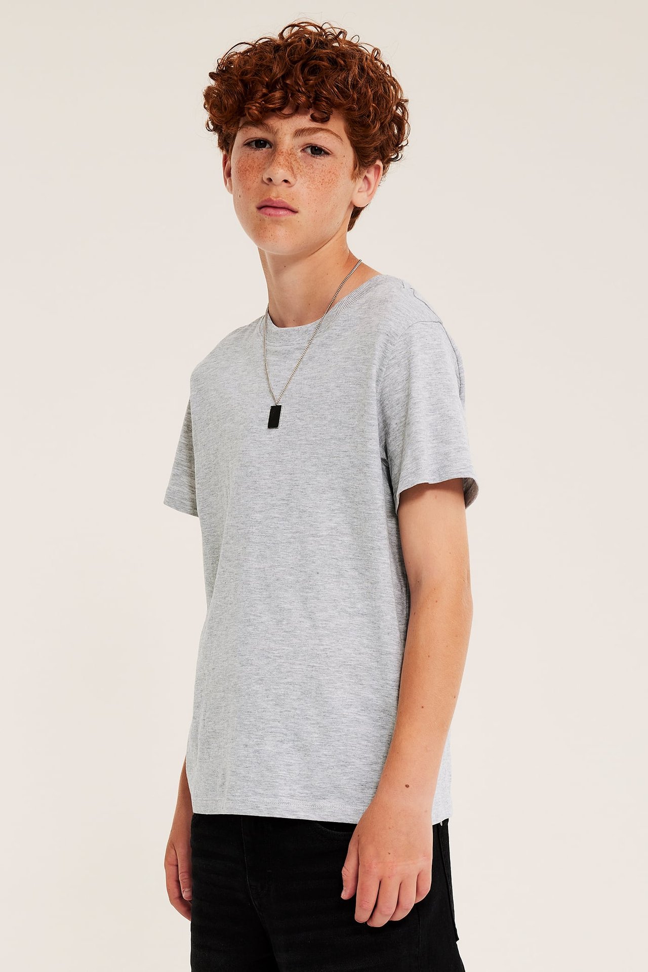 Framsida: barn bär en ljusgrå t-shirt, svarta byxor och ett silverhalsband.