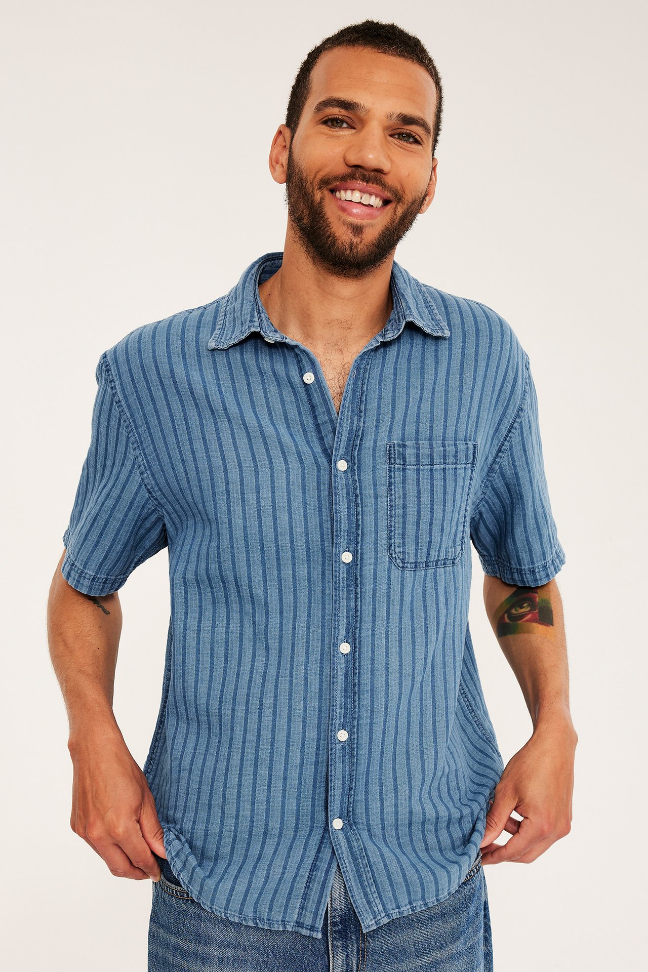 Front view: man i ljusblå randig kortärmad jeansskjorta med vita knappar och blå jeans.