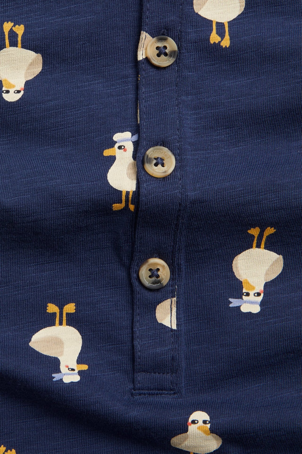 Zbliżenie na niebieski bawełniany pajacyk niemowlęcy w kaczki, z brązowymi guzikami.