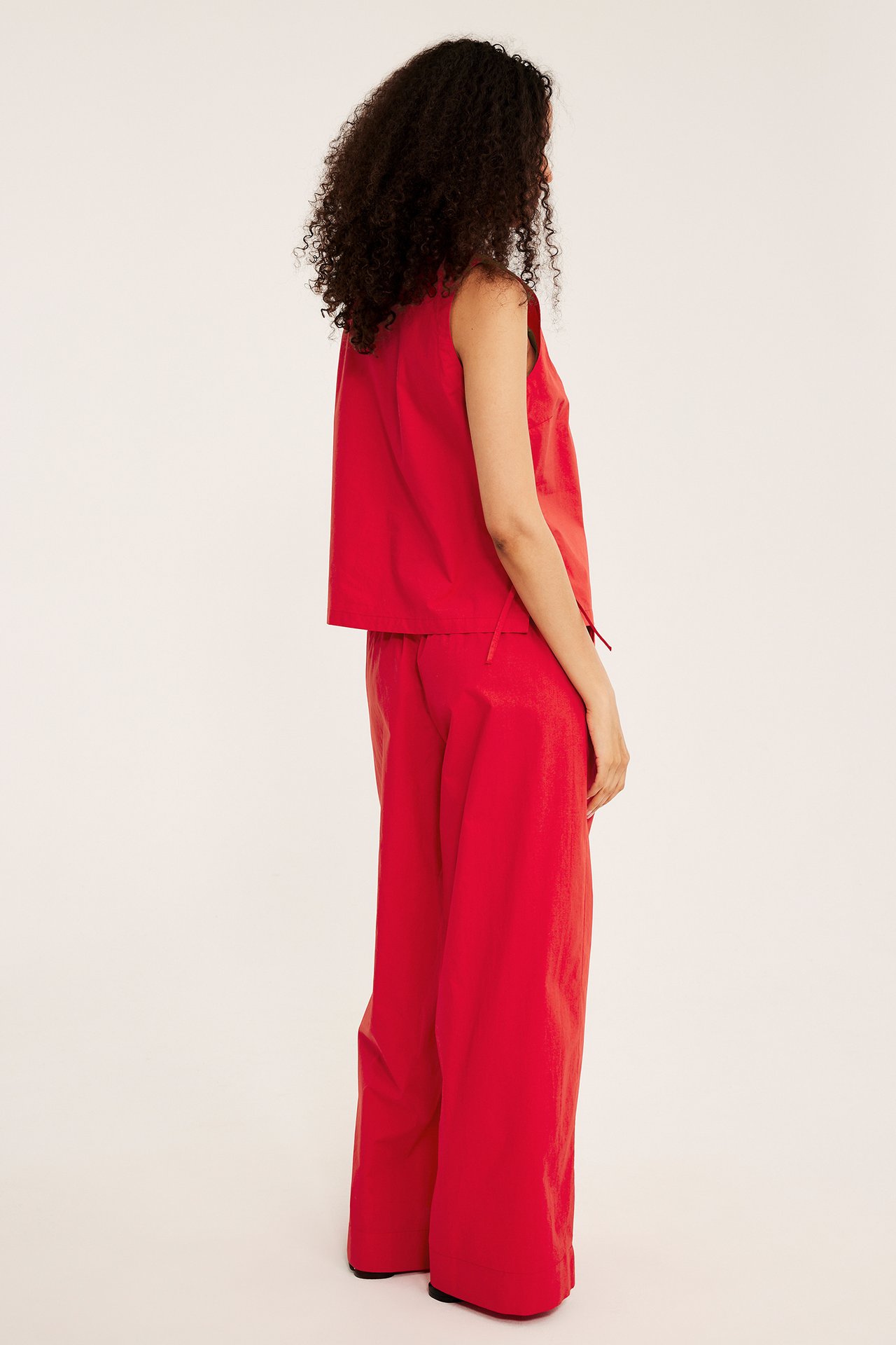 Sida vy av kvinna i röda vida bomullsbyxor och matchande röd ärmlös topp.