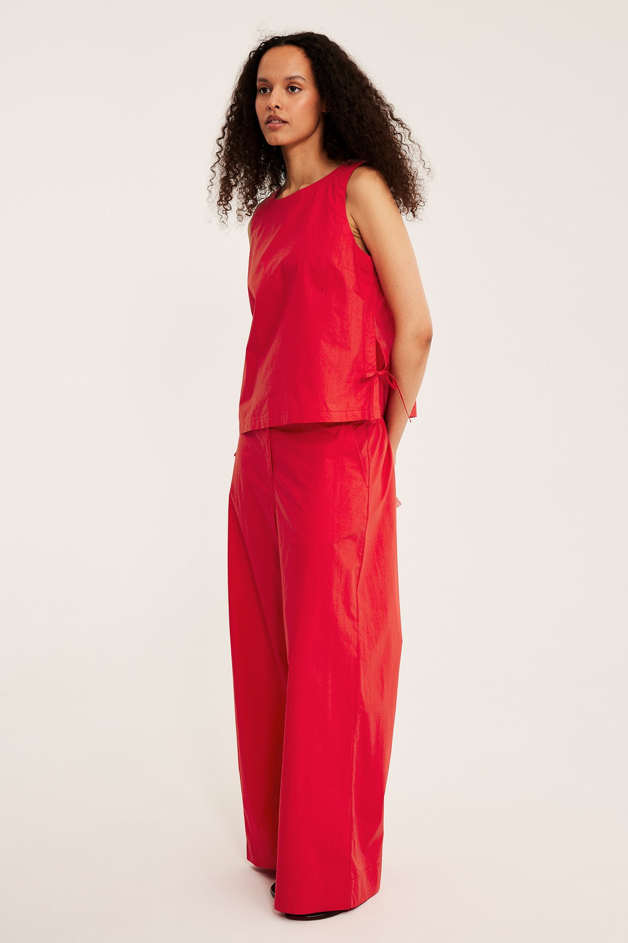 Framifrån: kvinna i vida röda bomullspoplinbyxor med fickor och matchande ärmlös topp.