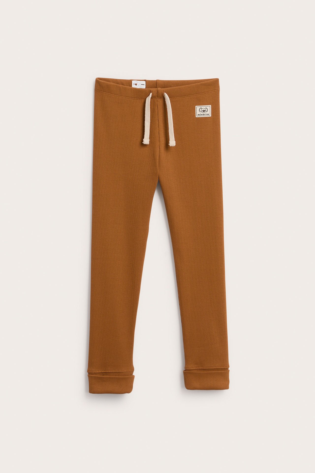 Framifrån, bruna ribbade barnleggings med krämfärgat dragsko och liten lapp.