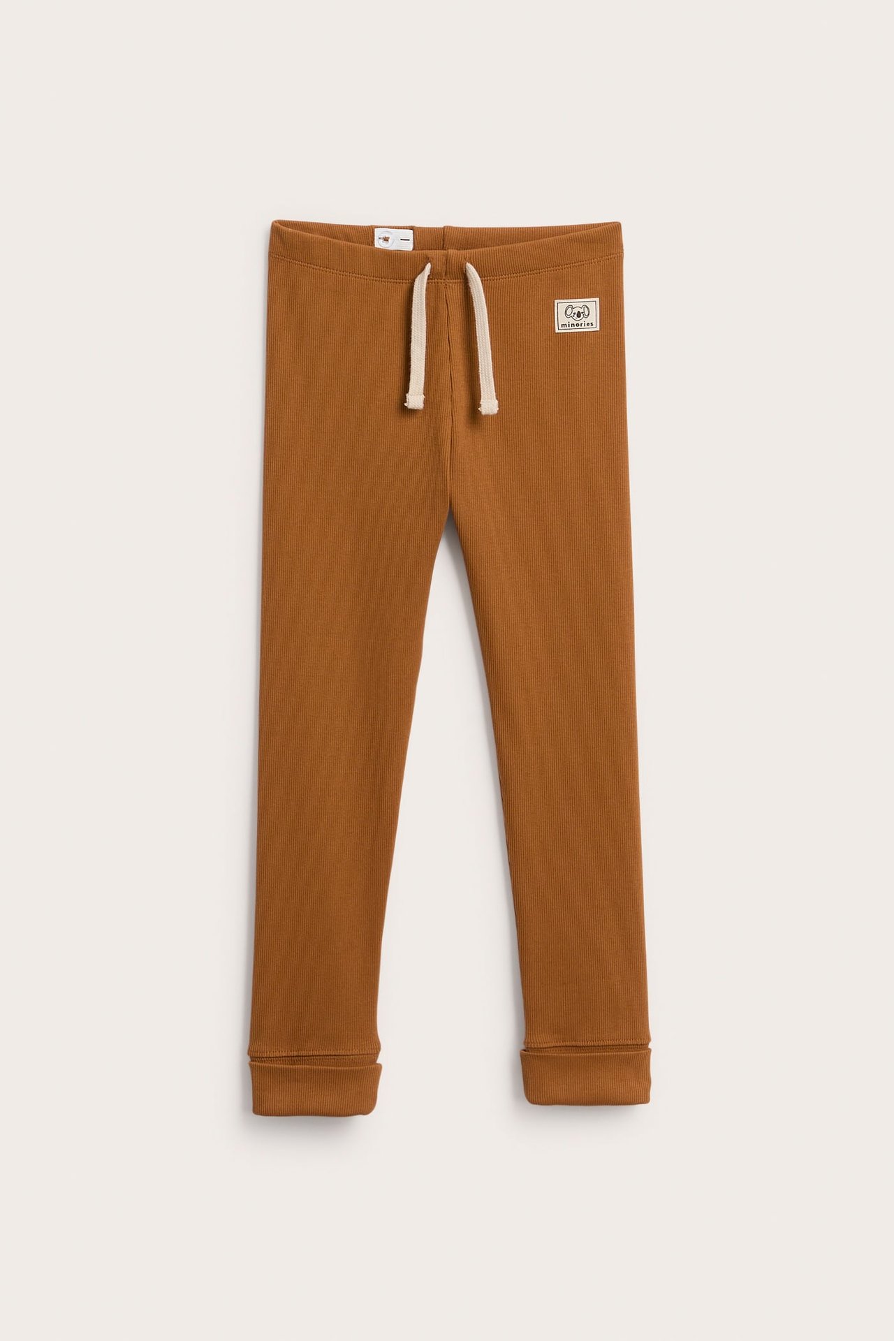 Front, brune ribbestrikkede barneleggings med kremfarget snøring og liten lapp.