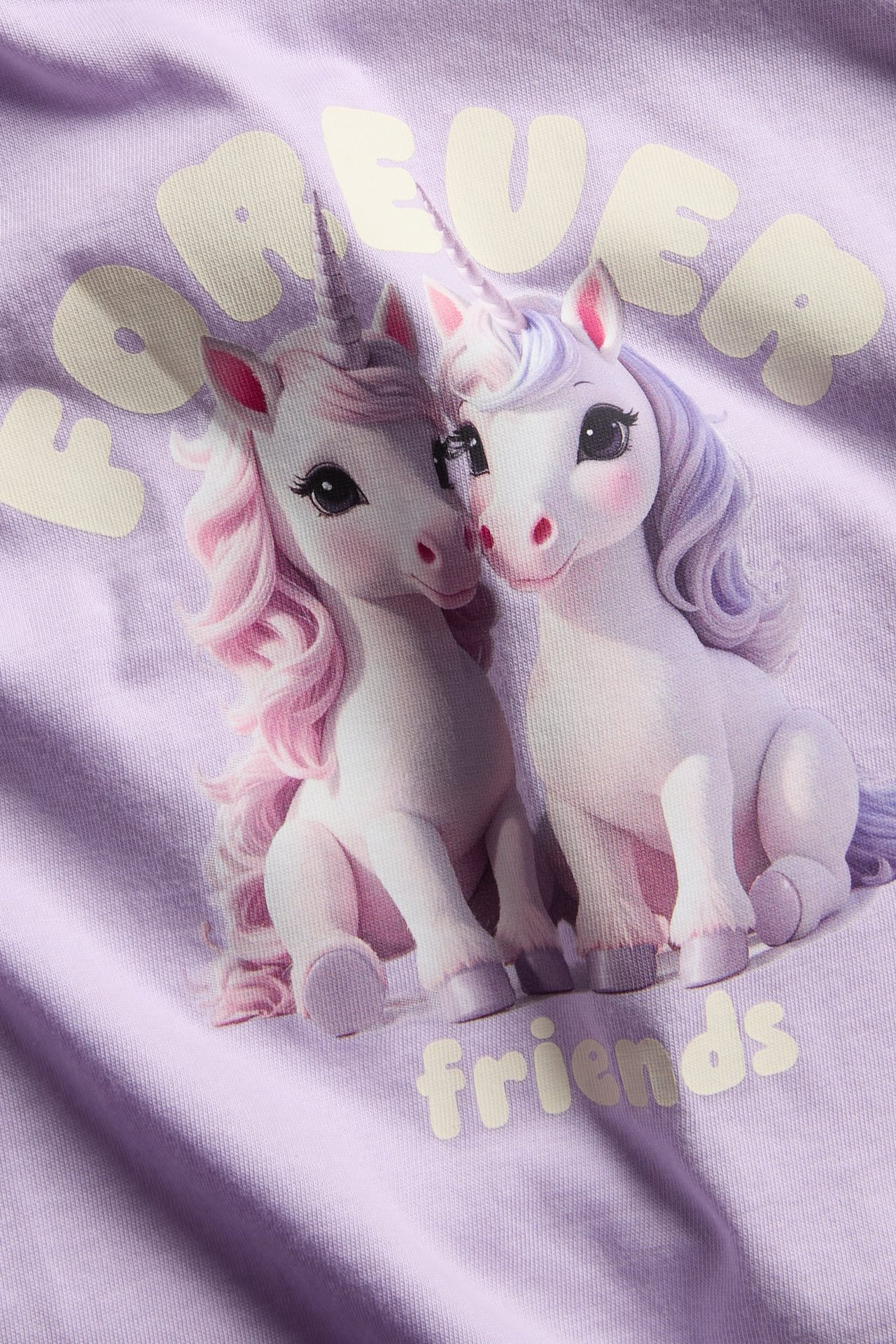 Nærbilde av et lyslilla plagg med trykk av to enhjørninger og teksten "FOREVER friends".