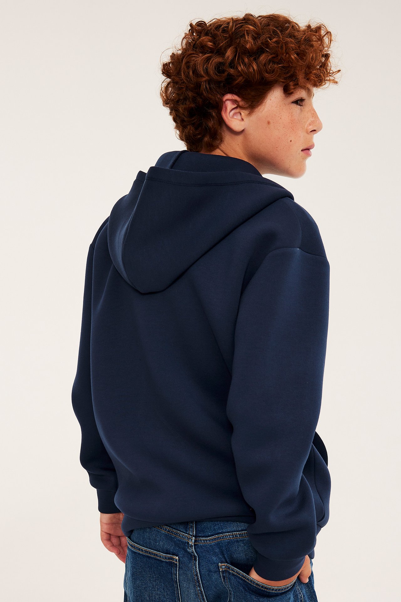 Sidovy på ett barn som bär en mörkblå huvtröja med luva och blå jeans.