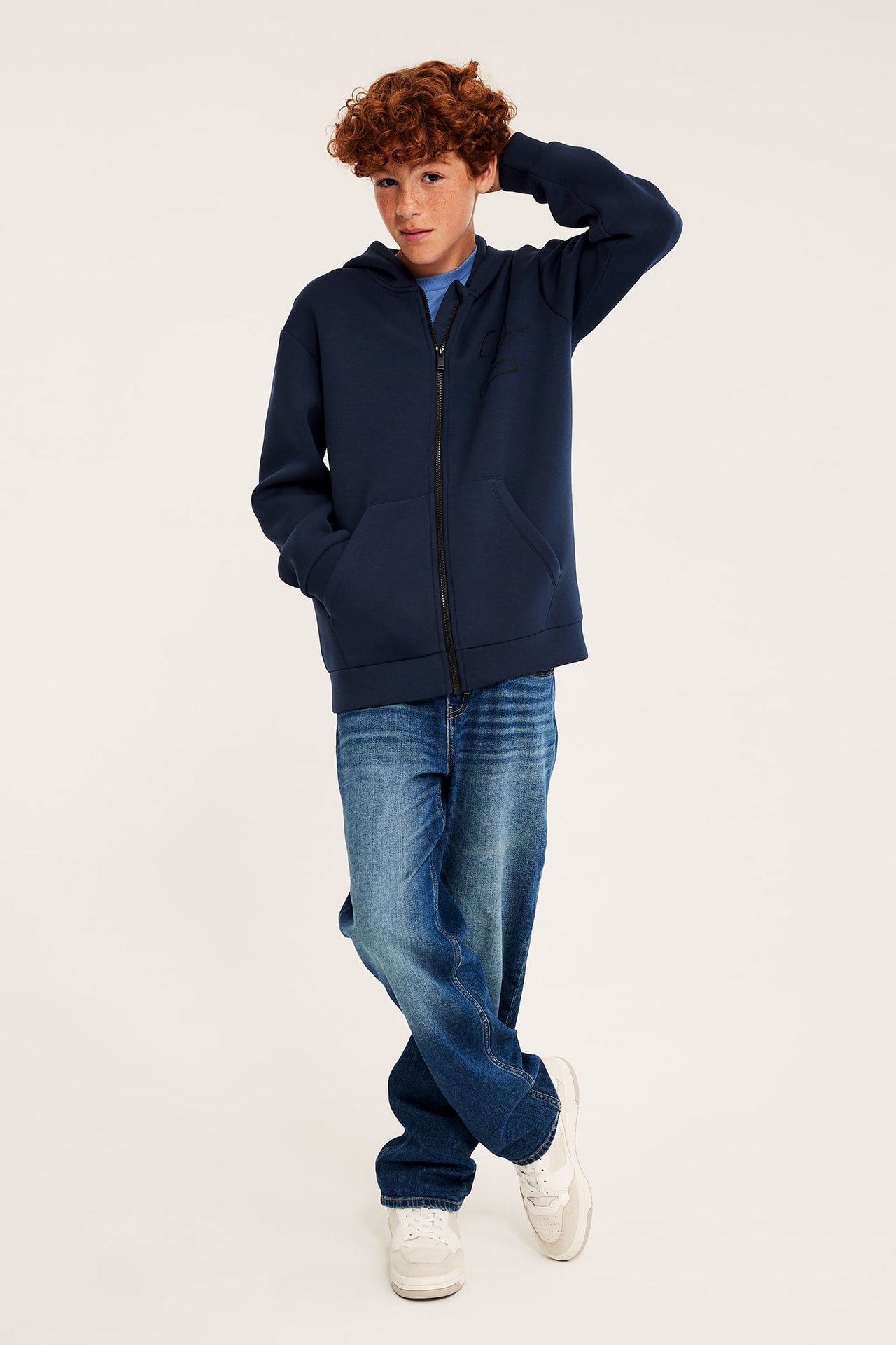 Frontbilde av barn i marineblå hettegenser med glidelås, blå t-skjorte, blå jeans og hvite joggesko.