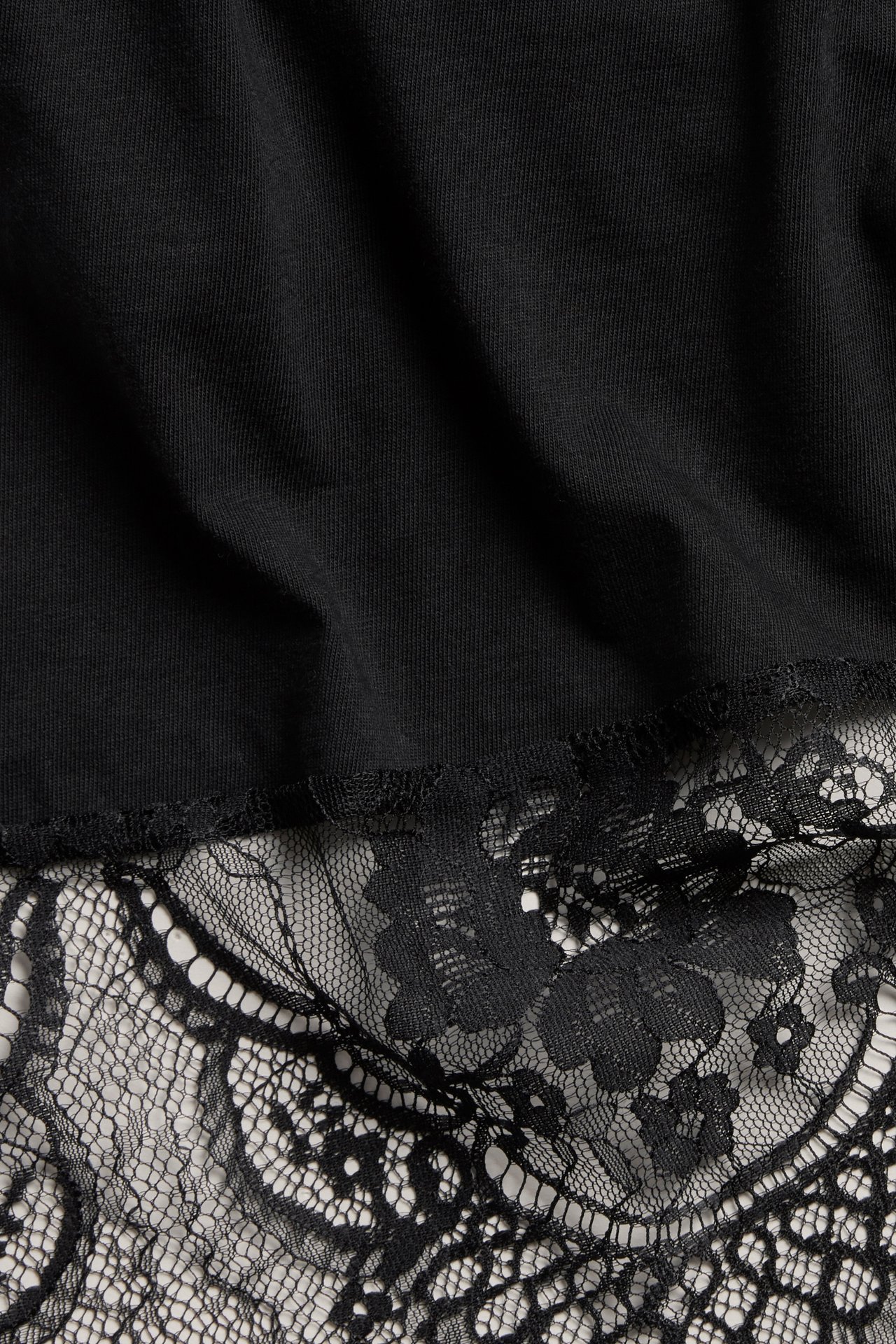 Lähikuva mustasta topista, jossa on epäsymmetrinen helma ja mustaa pitsiä.