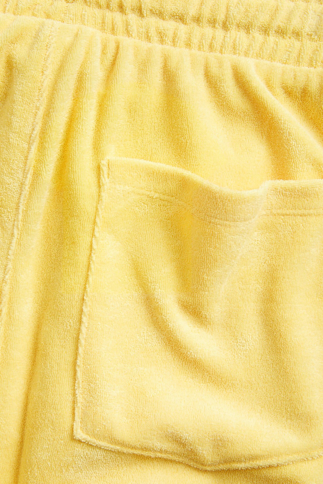 Lähikuva keltaisista froteeshortseista, joissa joustava kiristysnyörillinen vyötärö ja takatasku.