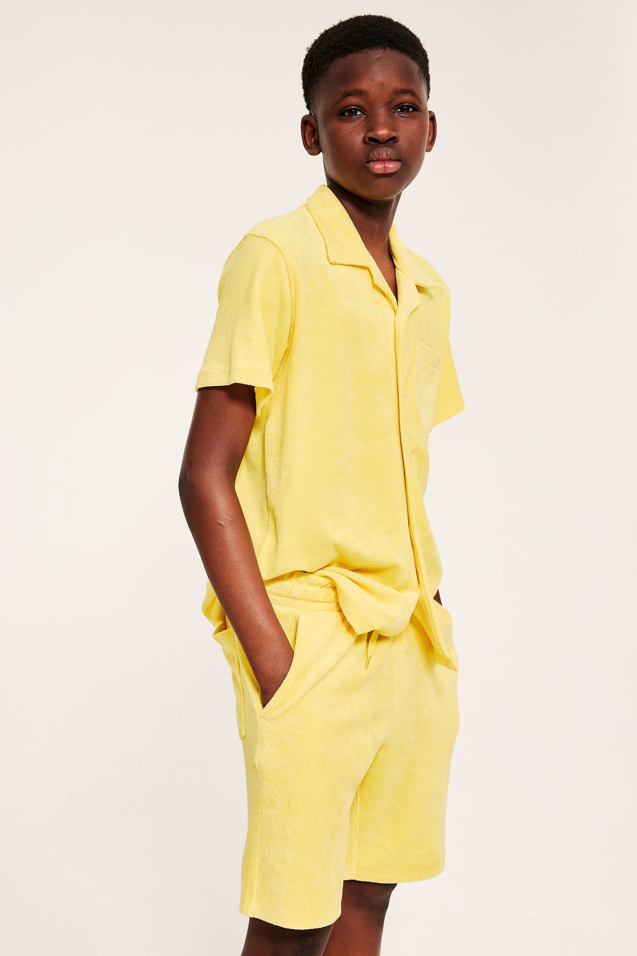 Widok z przodu dziecka w żółtych szortach frotte z troczkiem i pasującej koszuli.