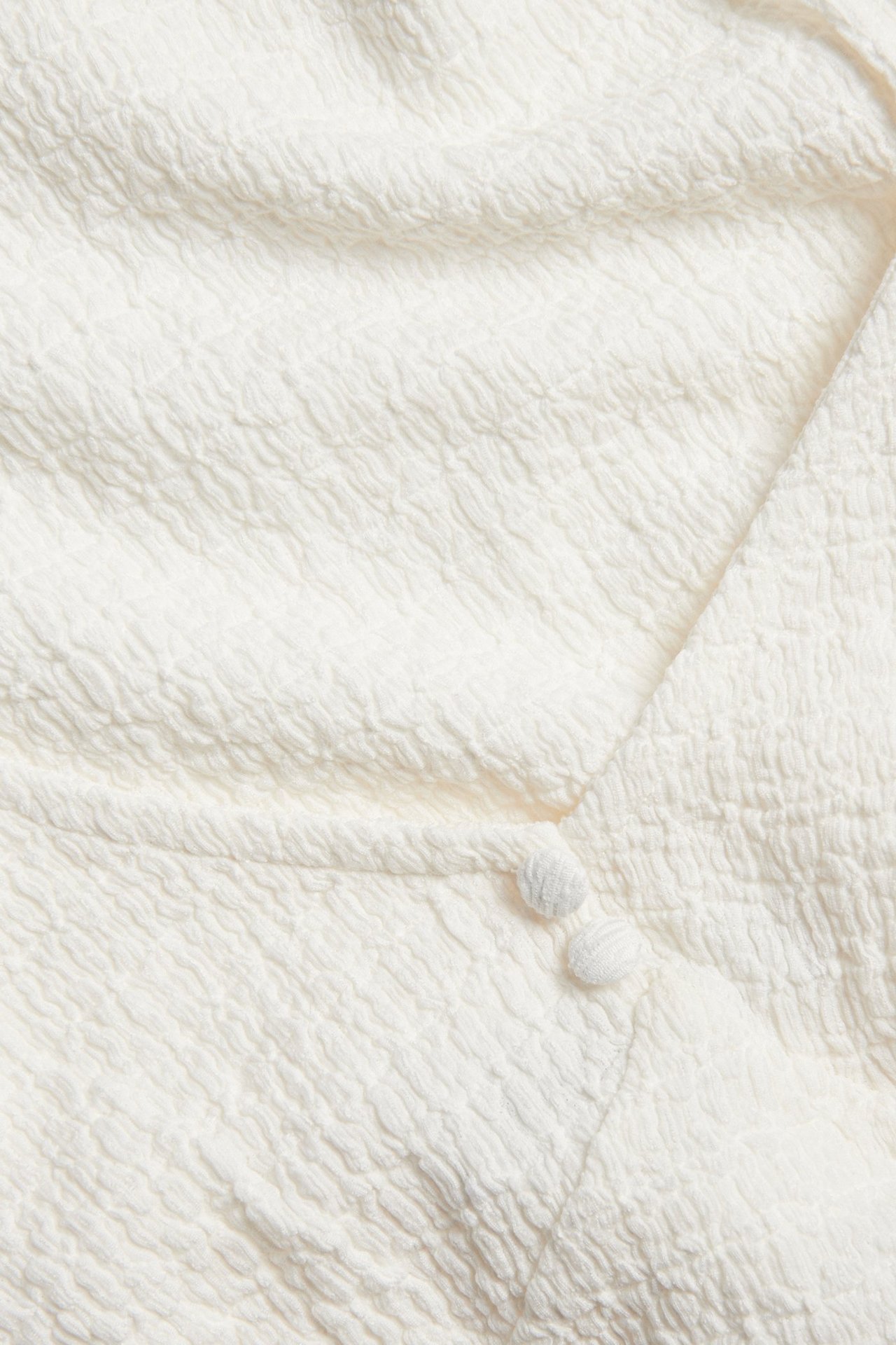 Nærbilde av en offwhite strukturert singlet med to matchende stofftrukne knapper.