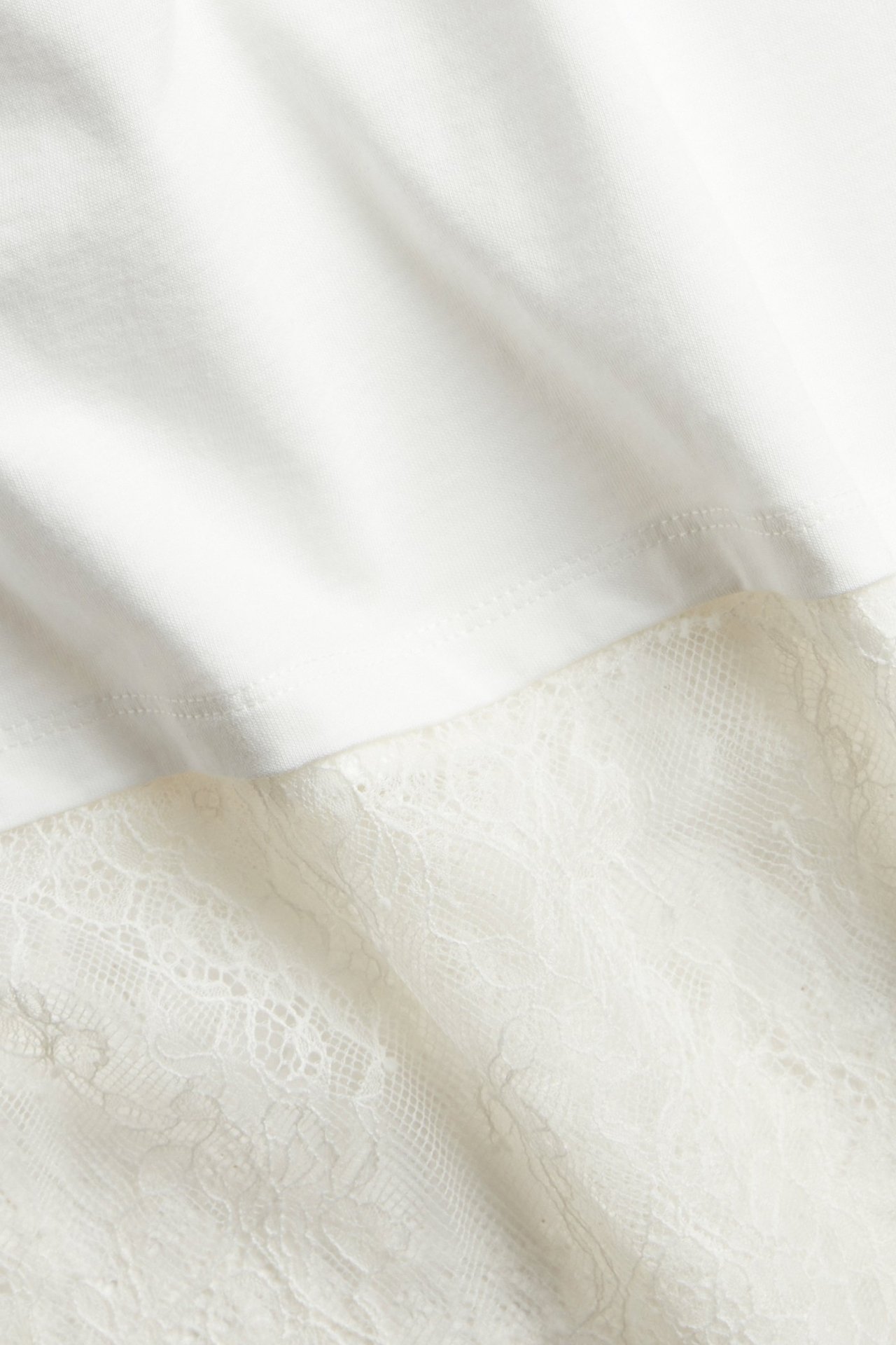 Zbliżenie na off-white'owy t-shirt z ozdobną koronkową lamówką u dołu.