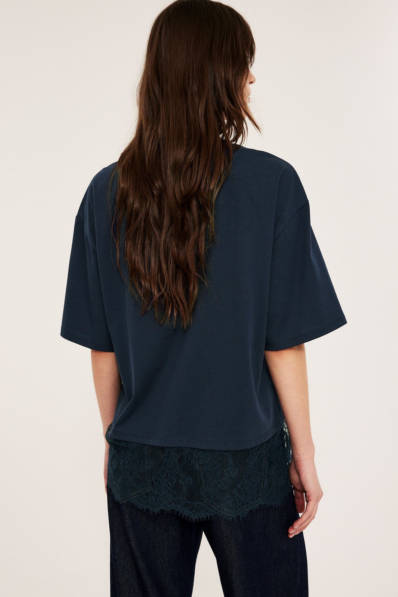 Bakfra: kvinne i løs mørkeblå t-skjorte med mørkeblå blondekant over mørke bukser.