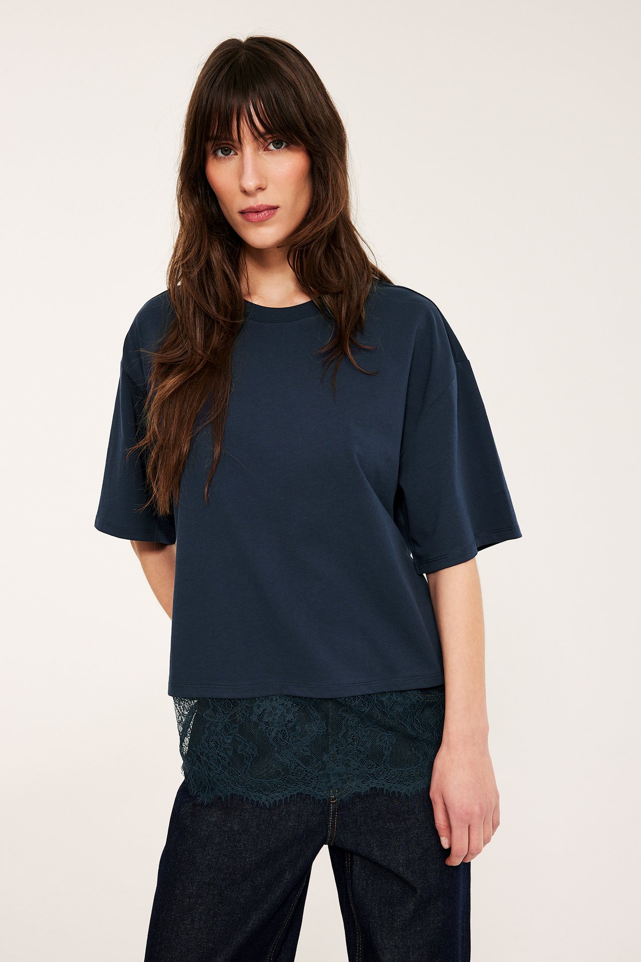 Framifrån, kvinna i lös mörkblå t-shirt med mörkgrön spetskant, stylad med mörkblå jeans.