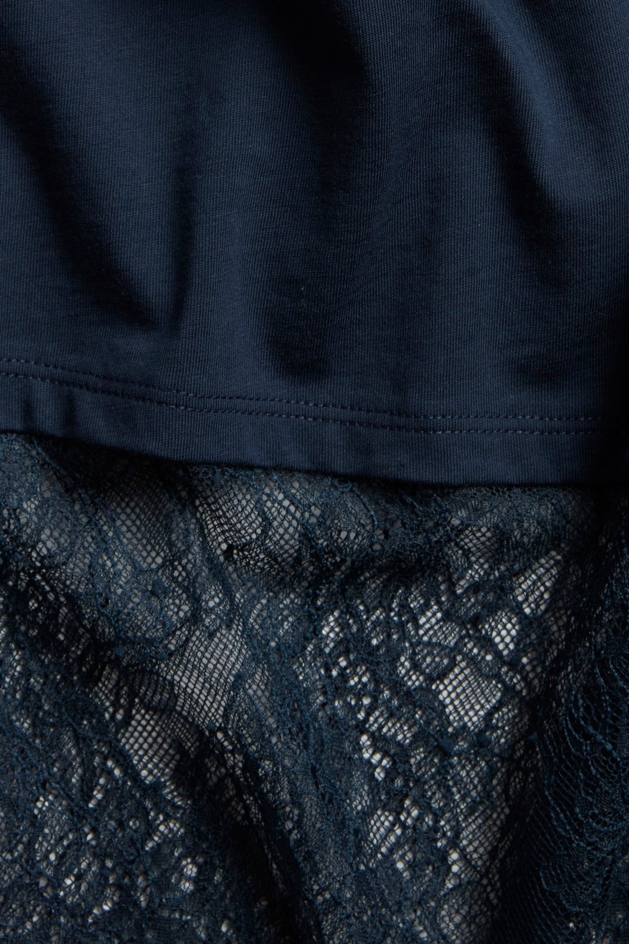 Zbliżenie na granatowy t-shirt z gładką górą i wzorzystą koronkową lamówką u dołu.
