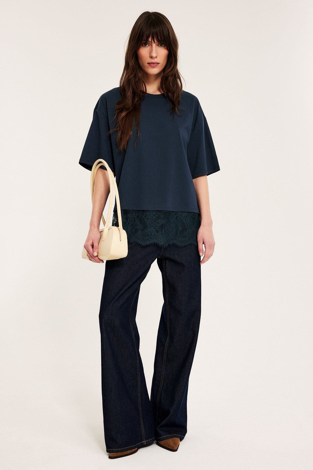 Z przodu: Kobieta w luźnym, granatowym t-shircie z zieloną koronką, granatowych dżinsach, z beżową torebką.