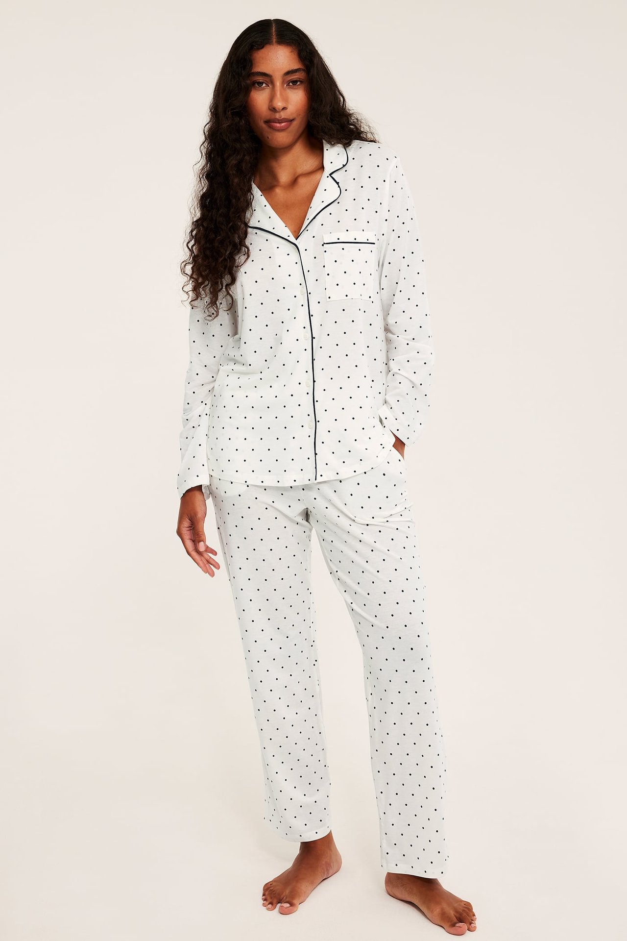 Frontalt bilde av kvinne i hvit prikkete pyjamas med svart passpoal.