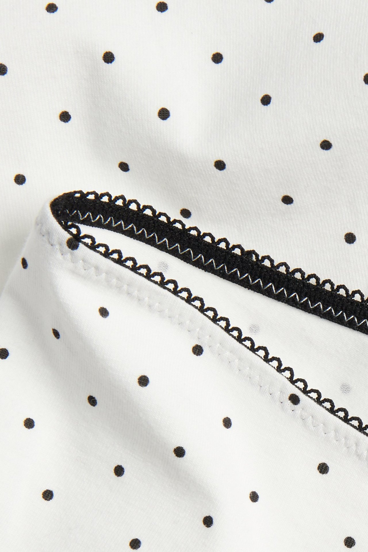 Närbild av off-white bomullsshortstrosor med svarta prickar och en svart picotkant.