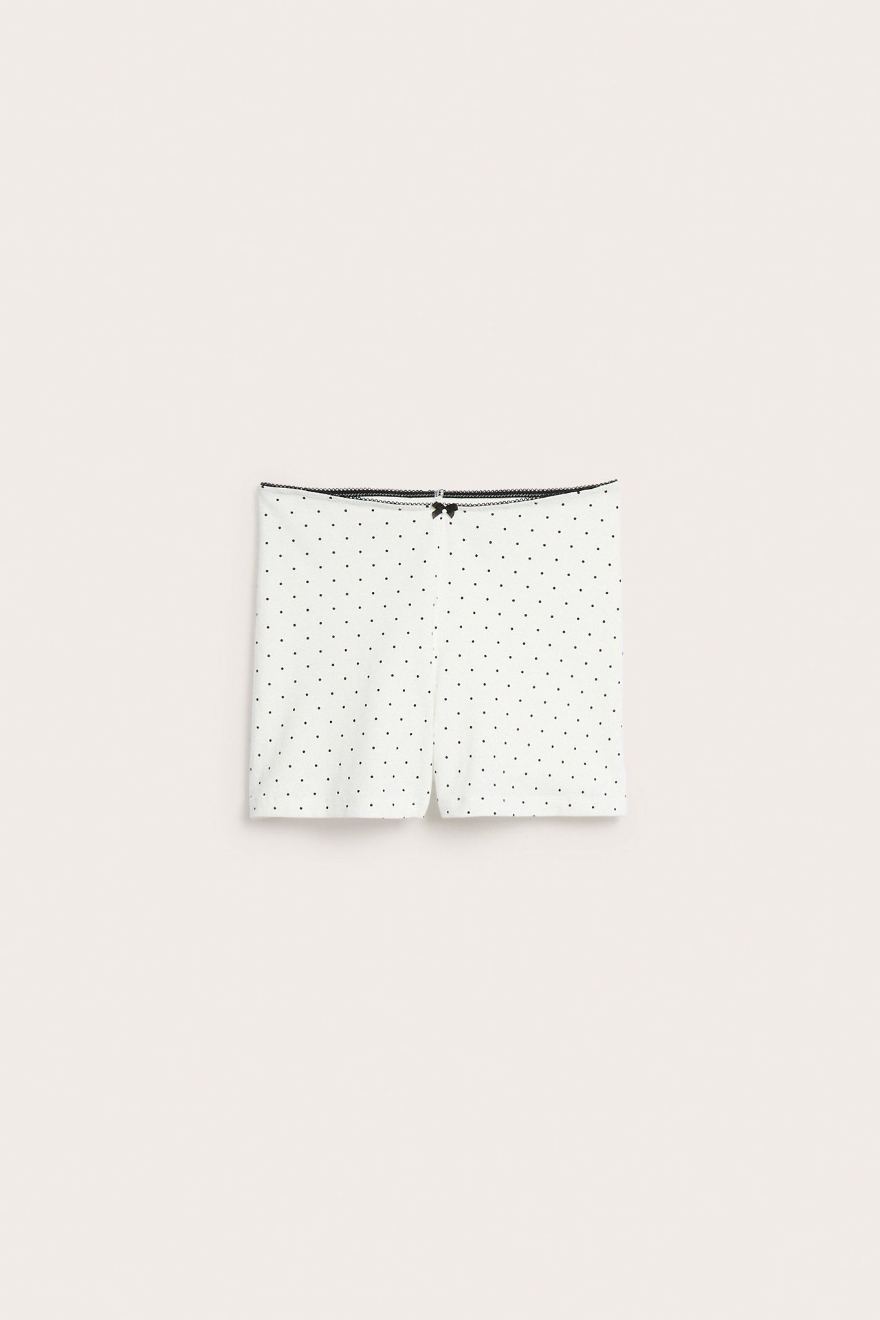 Framifrån, offwhite bomullsshorts med svarta prickar, picotkant och liten svart rosett.