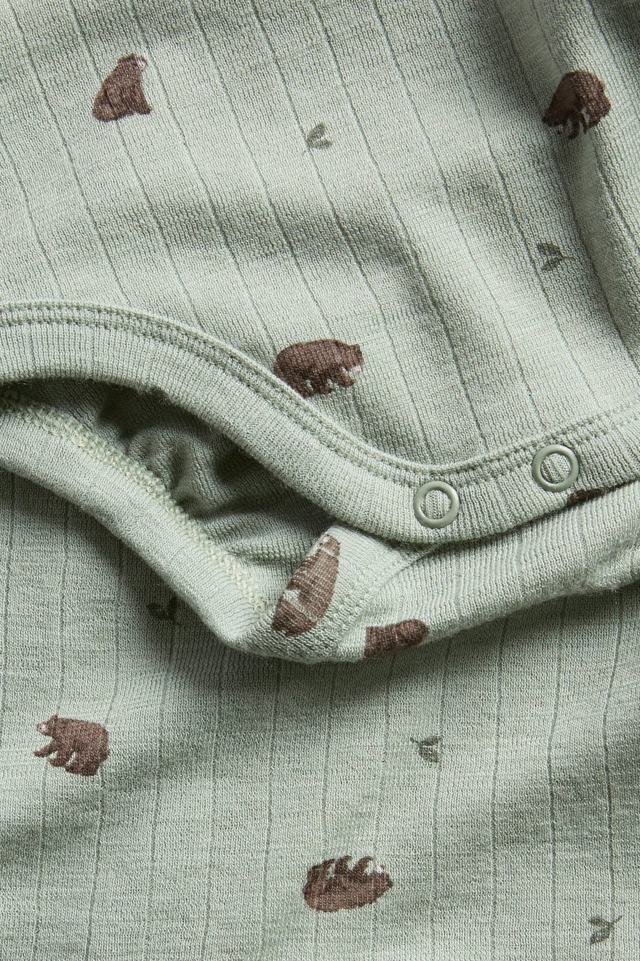 Närbild av en ljusgrön ribbad babybody med brunt björnmönster och två tryckknappar i grenen.