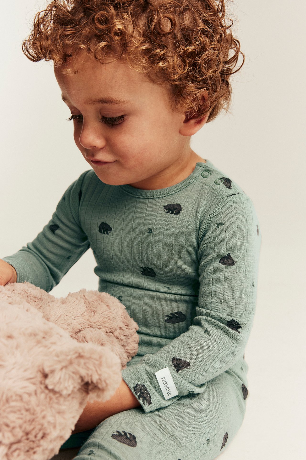 Babys salviagrön ribbad pyjamas med björntryck, tryckknappar på axeln, håller rosa mjukisdjur.