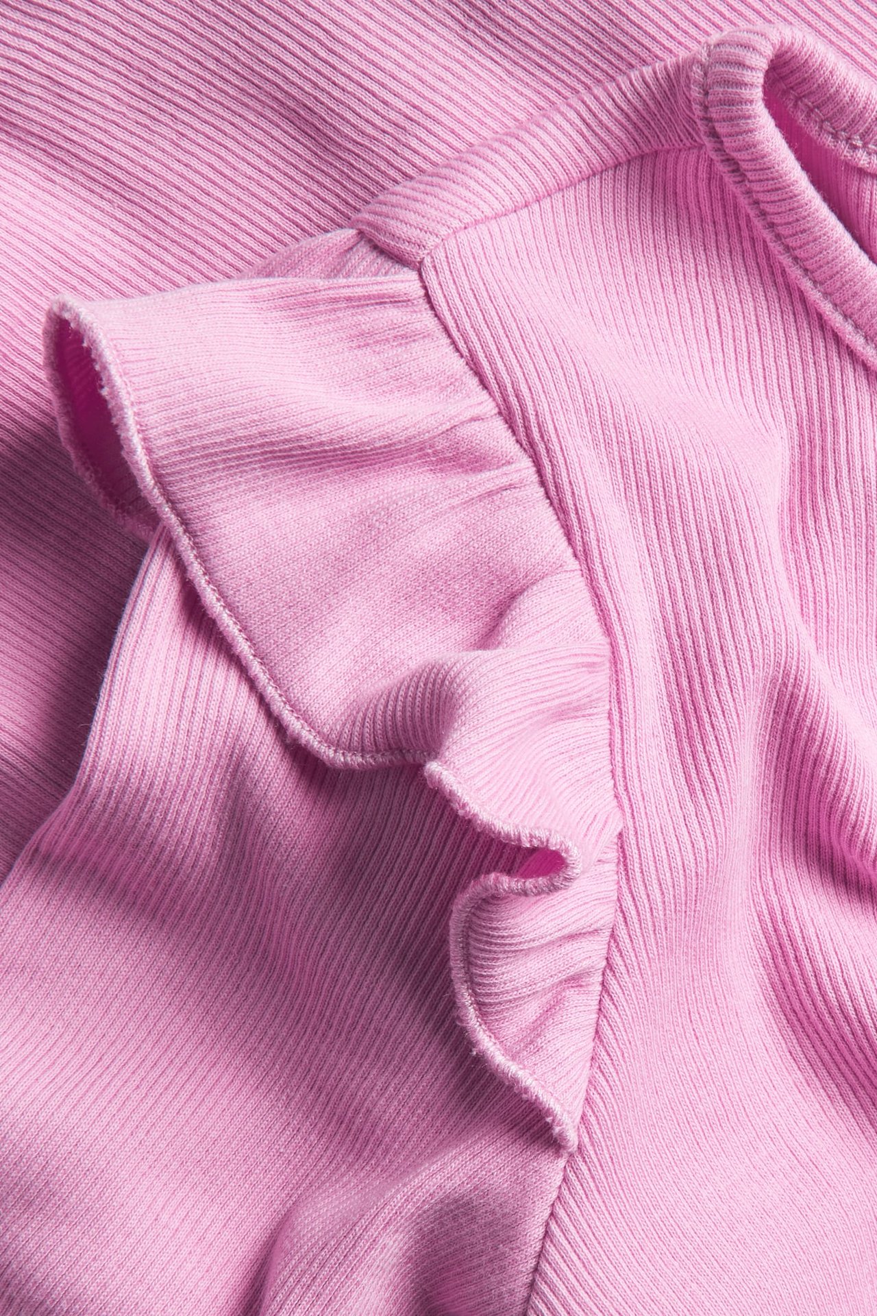 Lähikuva vaaleanpunaisesta ribbipaidasta, jossa on babylock-saumallinen röyhelö olkapäällä.