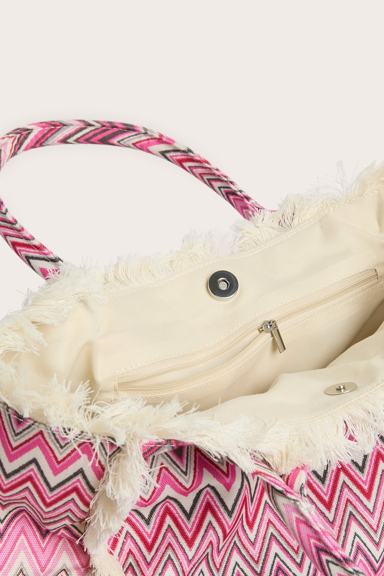 Zbliżenie na różową, kremową i czarną torbę z tkaniny w zygzak z frędzlami i zapięciem magnetycznym.