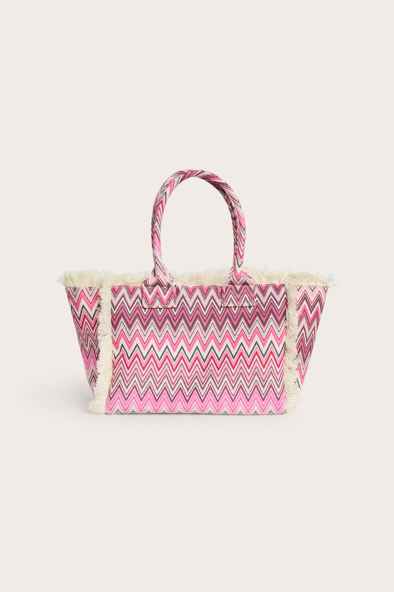 Edestä näkymä kangaskassista, jossa vaaleanpunainen, valkoinen ja tumma siksak-kuvio sekä luonnonvalkoiset hapsut.