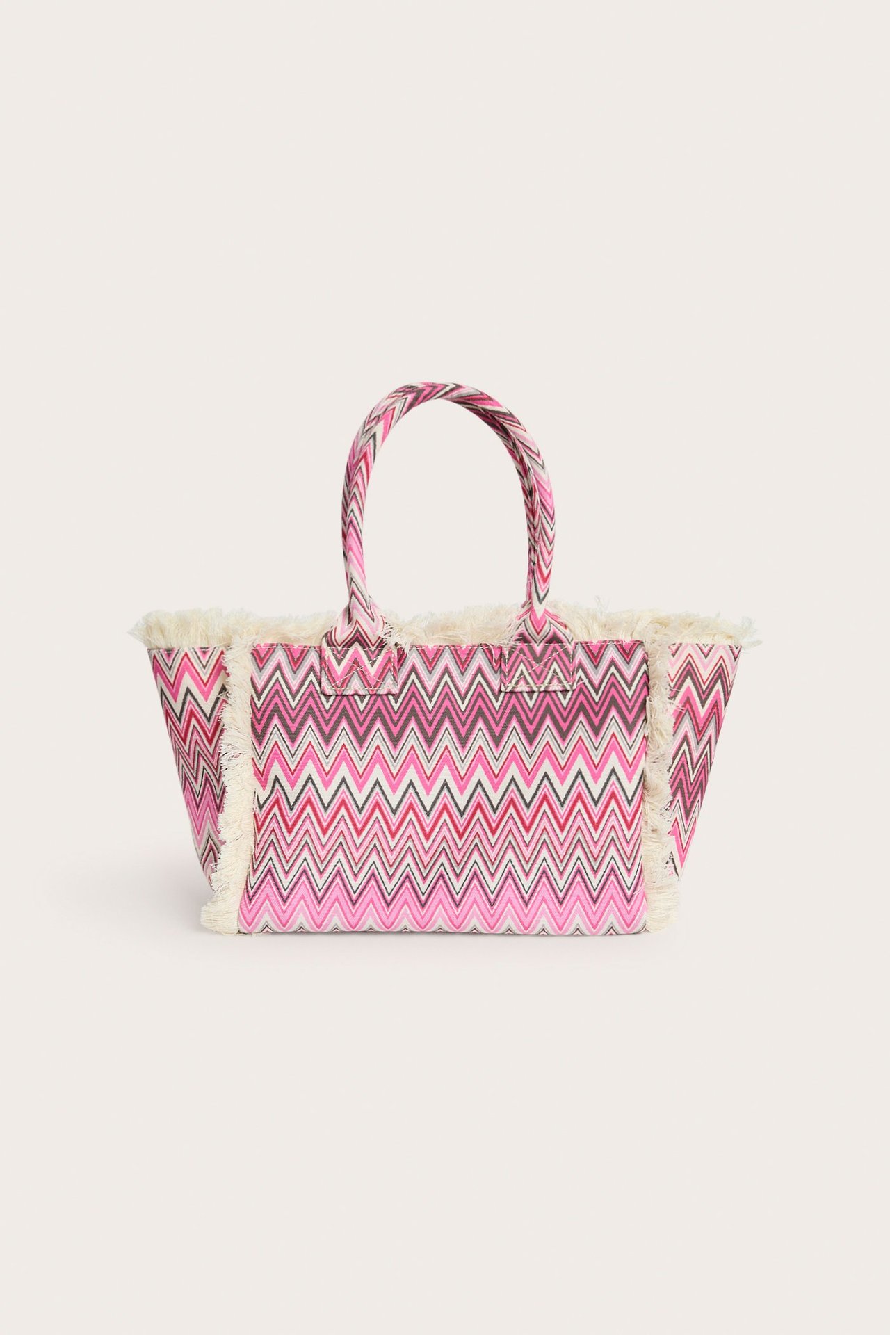 Edestä näkymä kangaskassista, jossa vaaleanpunainen, valkoinen ja tumma siksak-kuvio sekä luonnonvalkoiset hapsut.