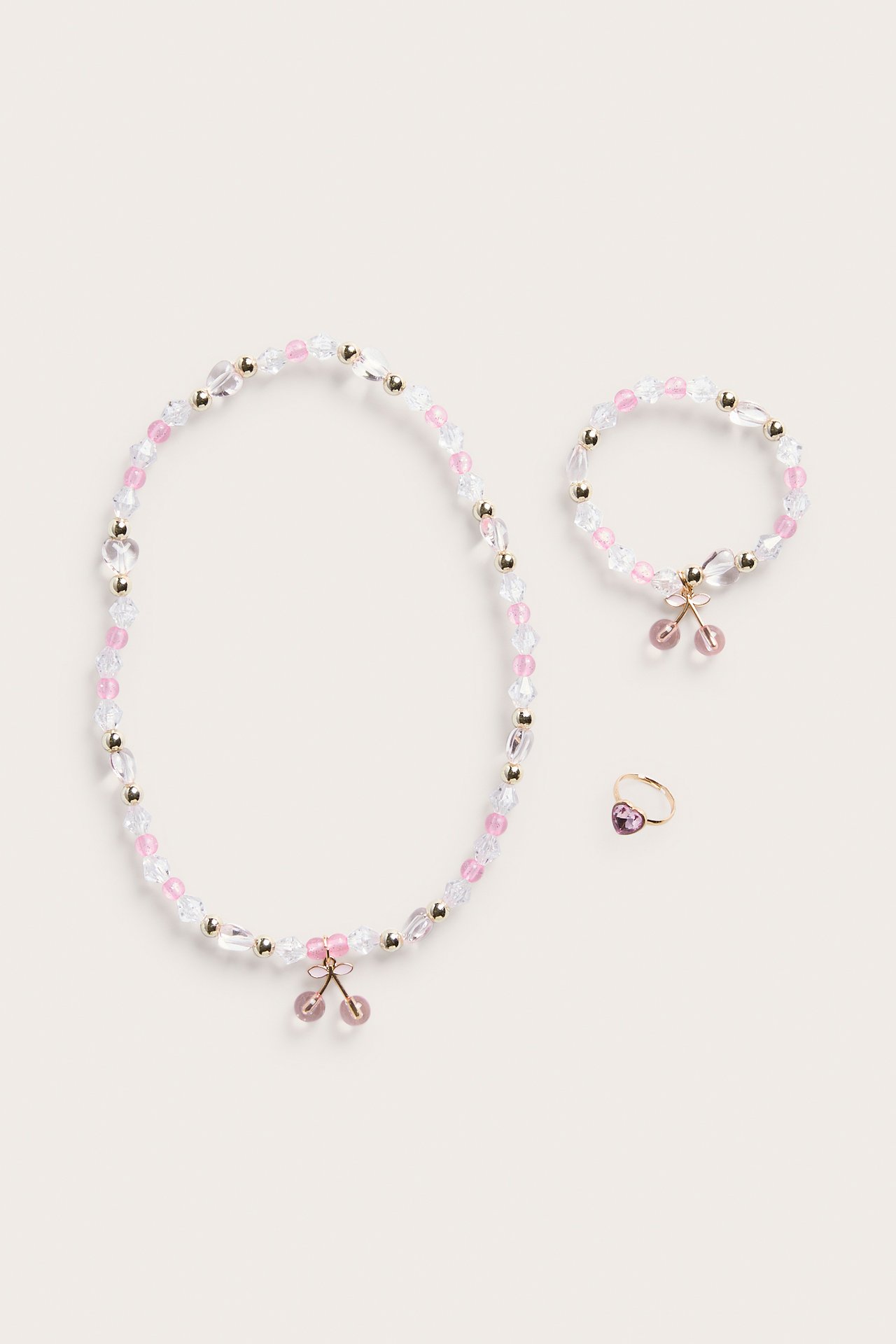 Från ovan: rosa och klara pärlhalsband med körsbärsberlock, matchande armband och rosa hjärtring.