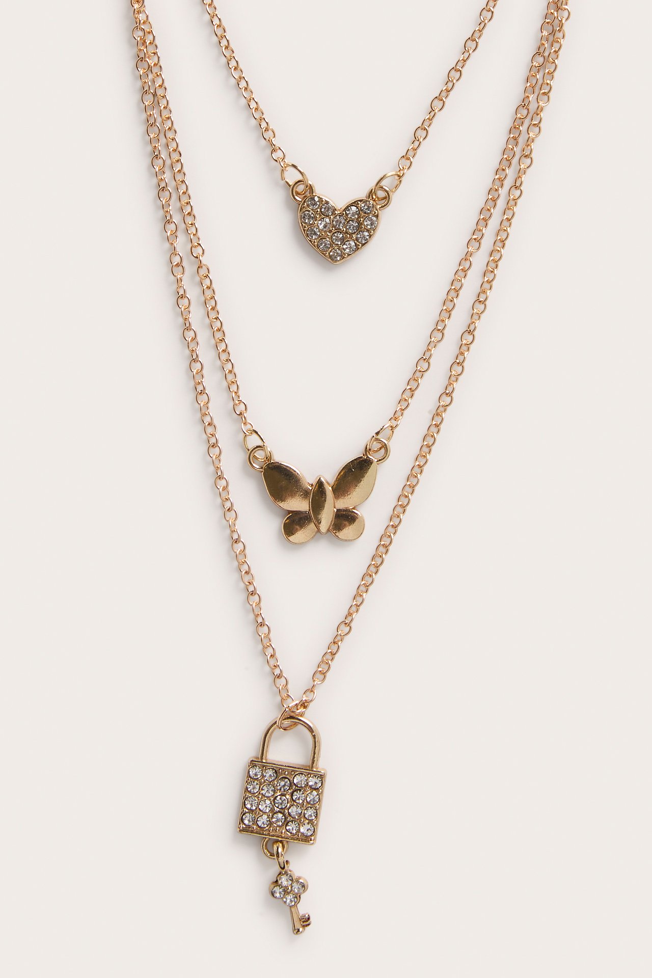 Lähikuva: kullanvärinen kolmikerroksinen kaulakoru, jossa strassihertta, perhonen sekä strassilukko avaimella.