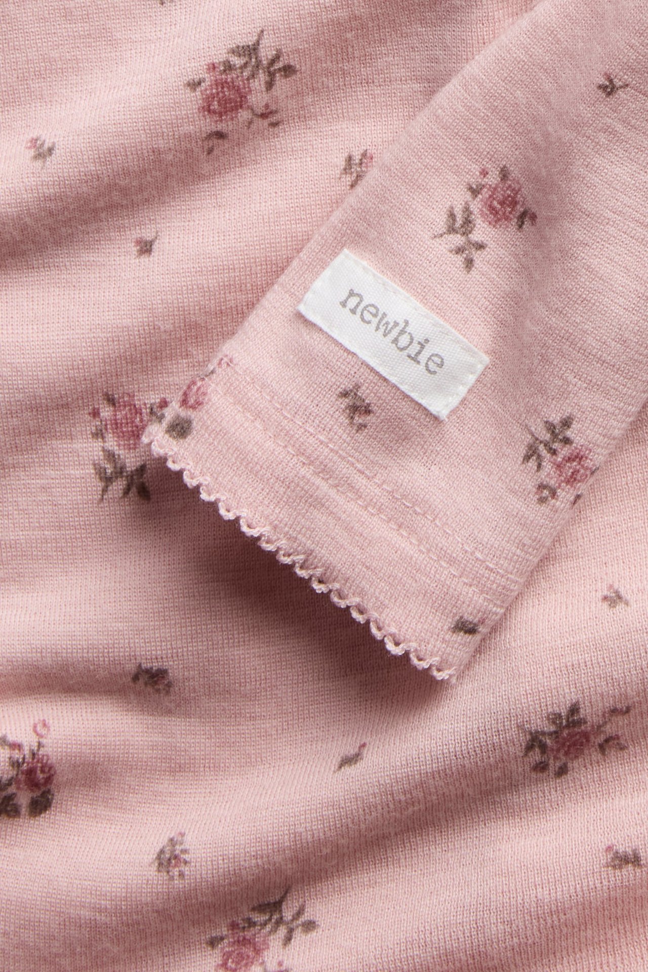 Nærbilde av et rosa langermet strikket babyplagg med blomstermønster og bølgete kant.