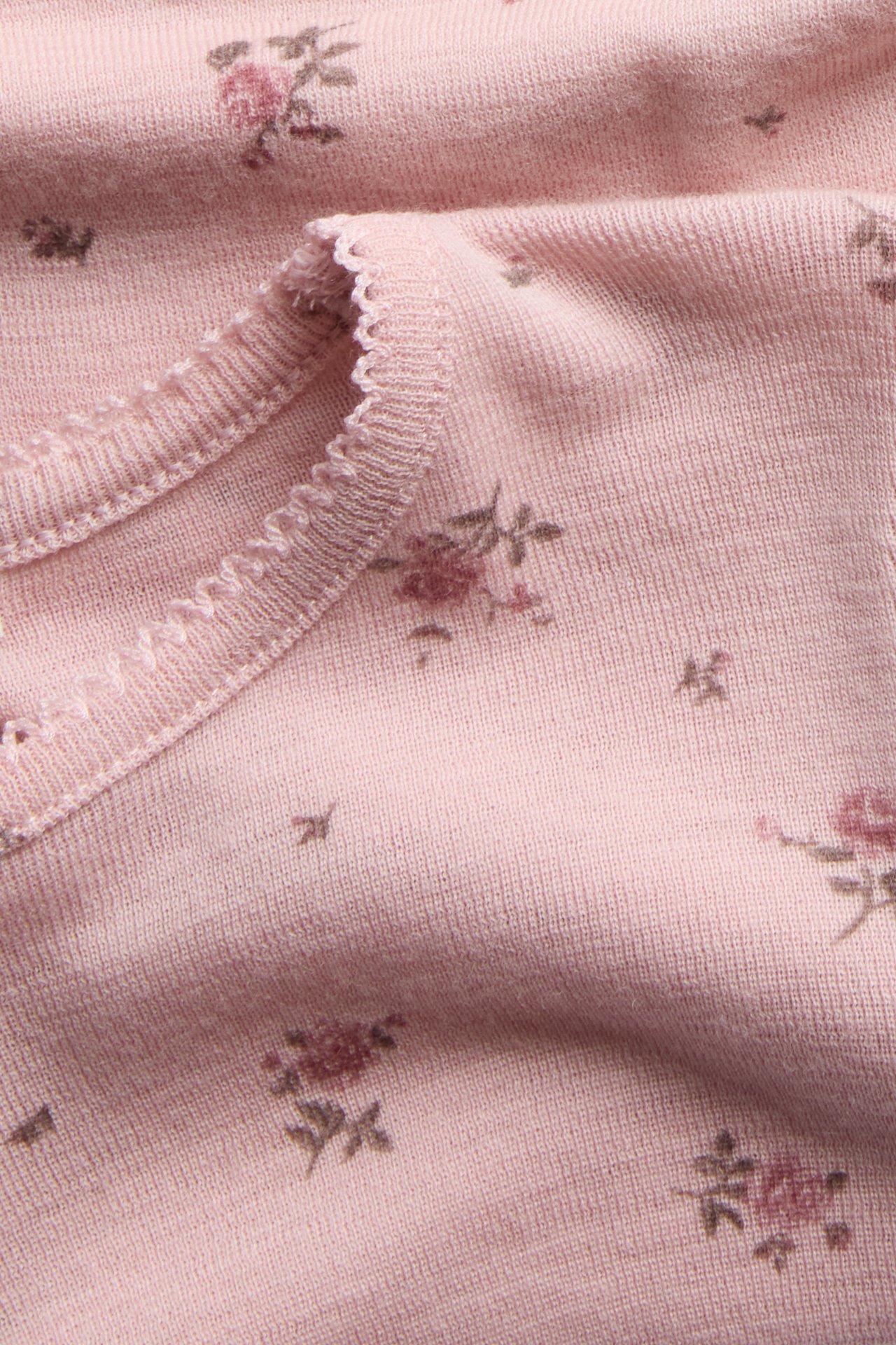 Nærbilde av en rosa strikket topp med delikat blomstertrykk og rynket kant.