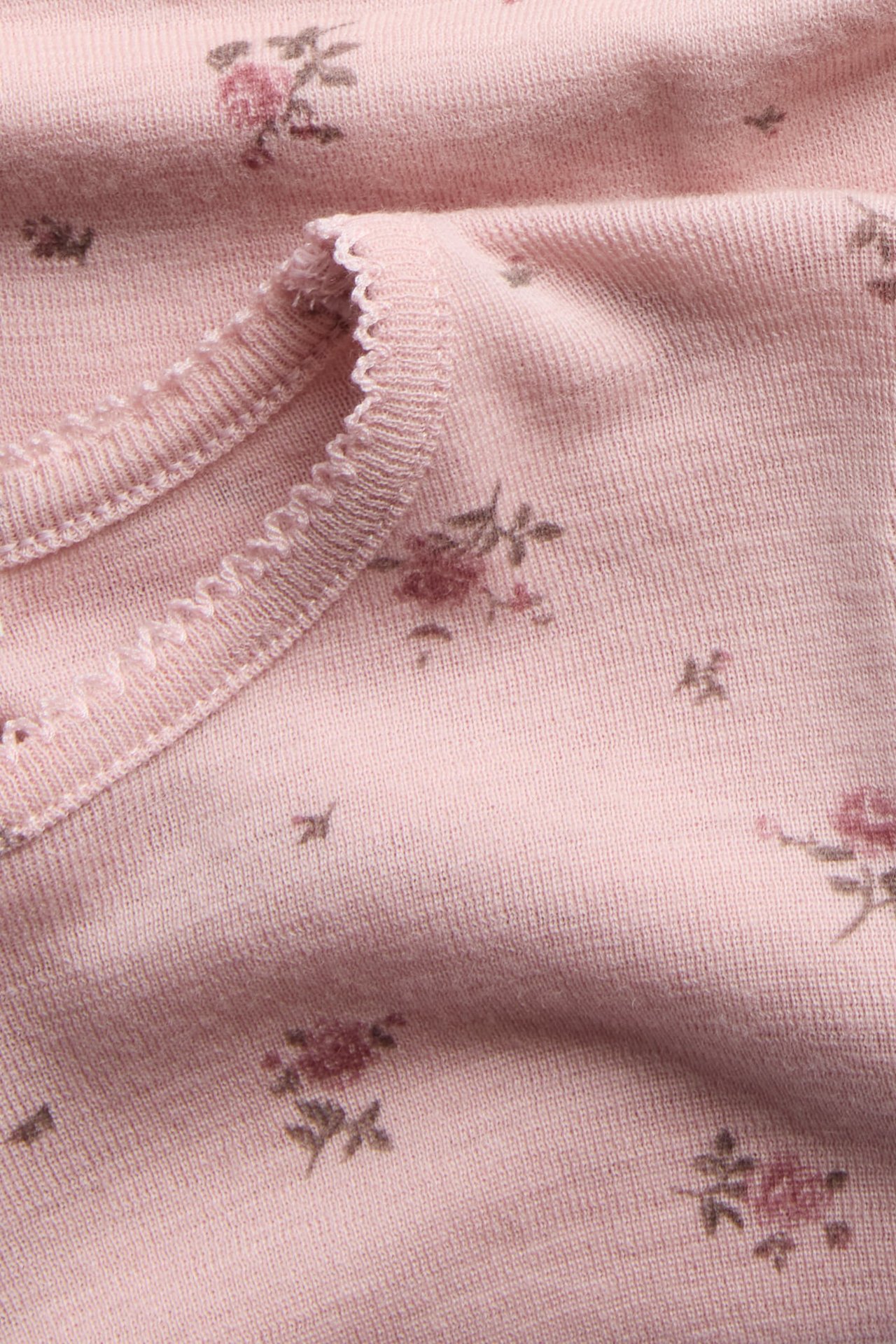 Nærbilde av en rosa strikket topp med delikat blomstertrykk og rynket kant.