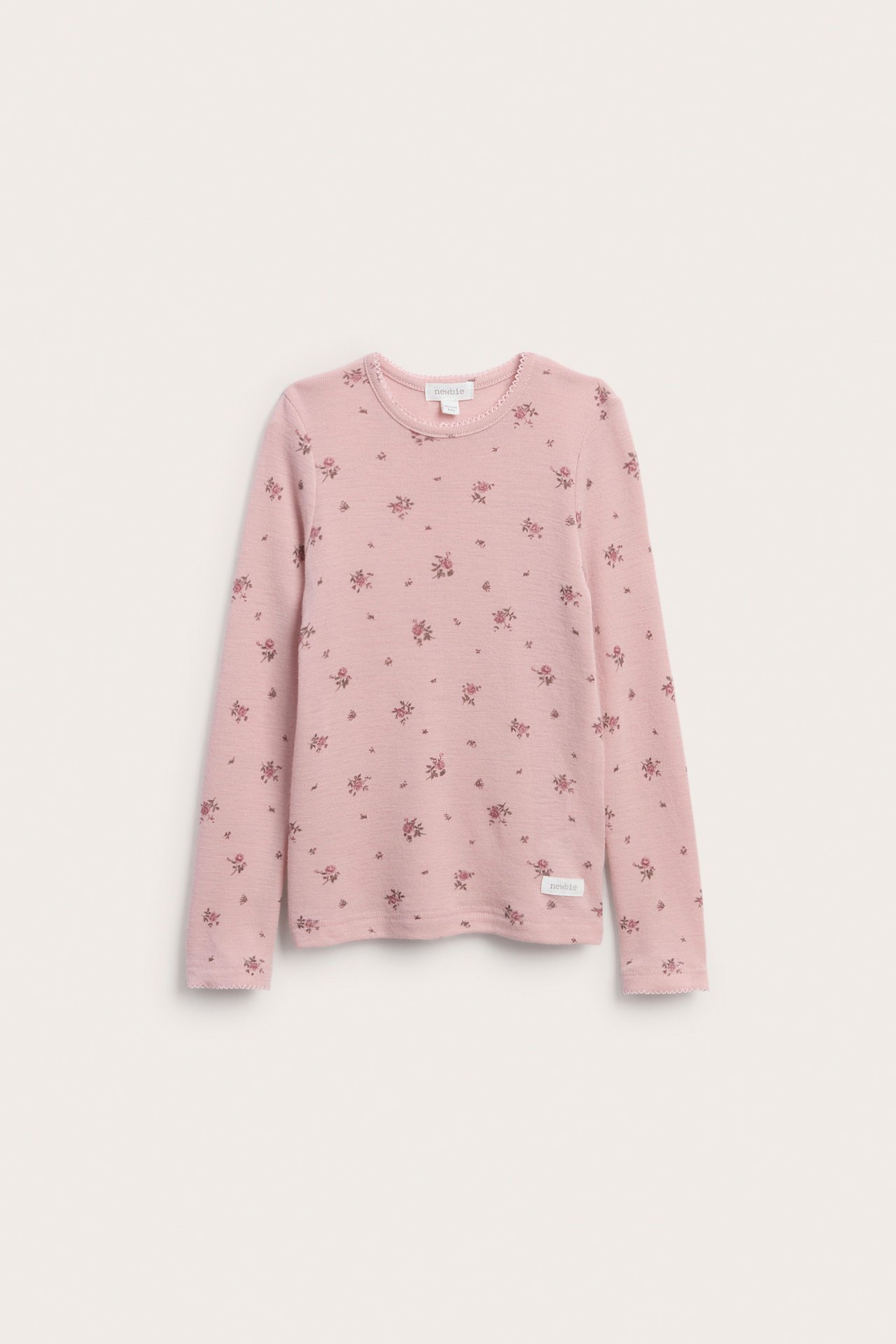 Forfra en rosa langermet barnegenser med et lite blomstermønster og bølgete kant.