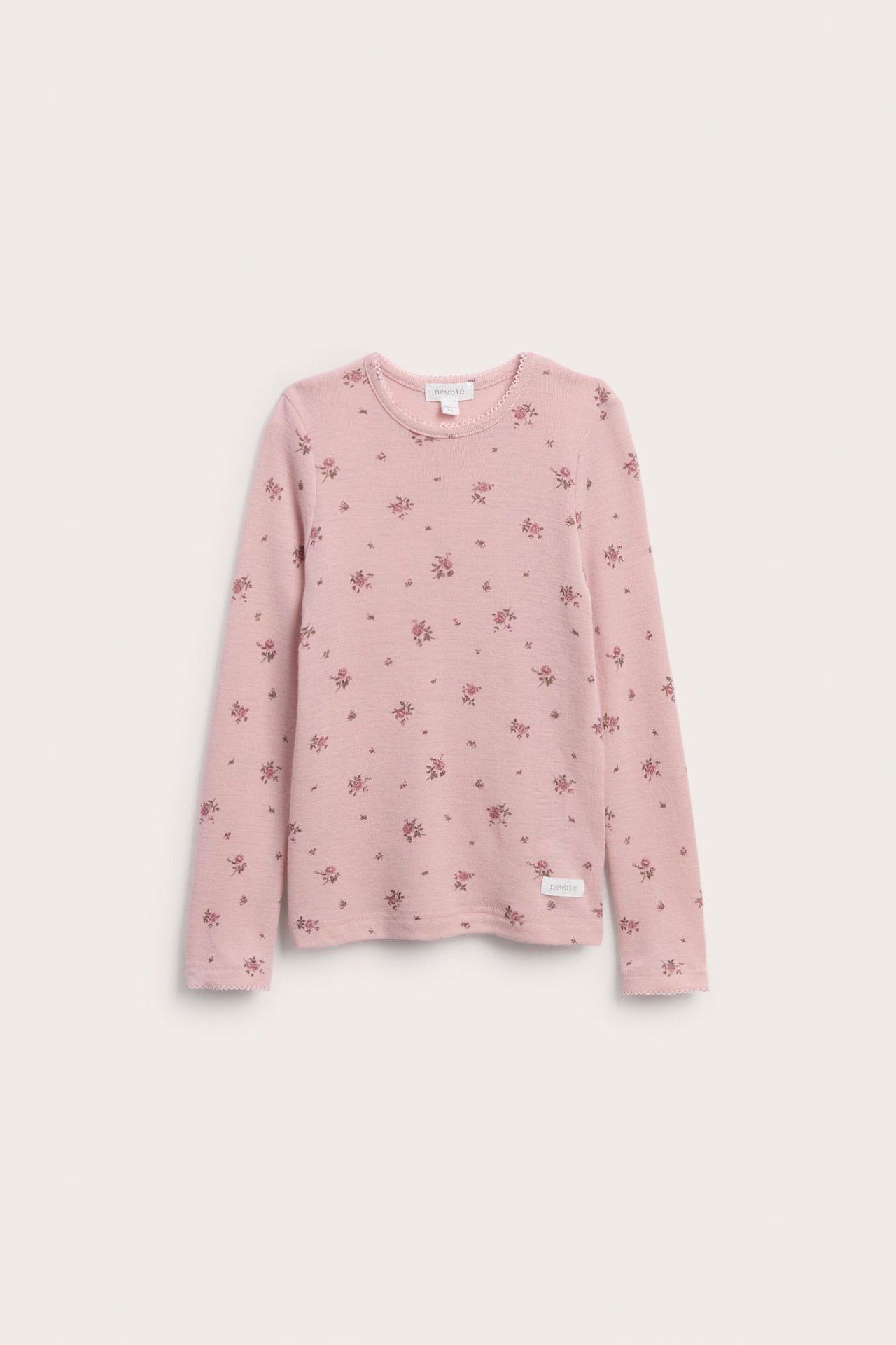 Forfra en rosa langermet barnegenser med et lite blomstermønster og bølgete kant.