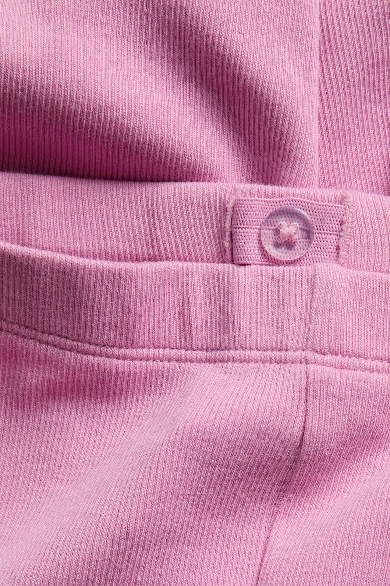 Nærbilde av rosa ribbestrikkede leggings som viser det justerbare elastiske midjebåndet med en klar knapp.
