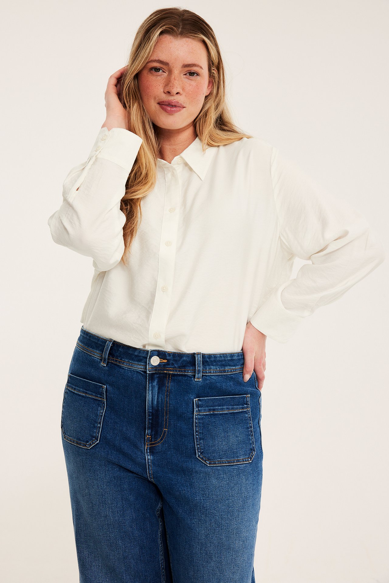 Frontbilde av en kvinne med en hvit langermet skjorte og blå vide jeans.