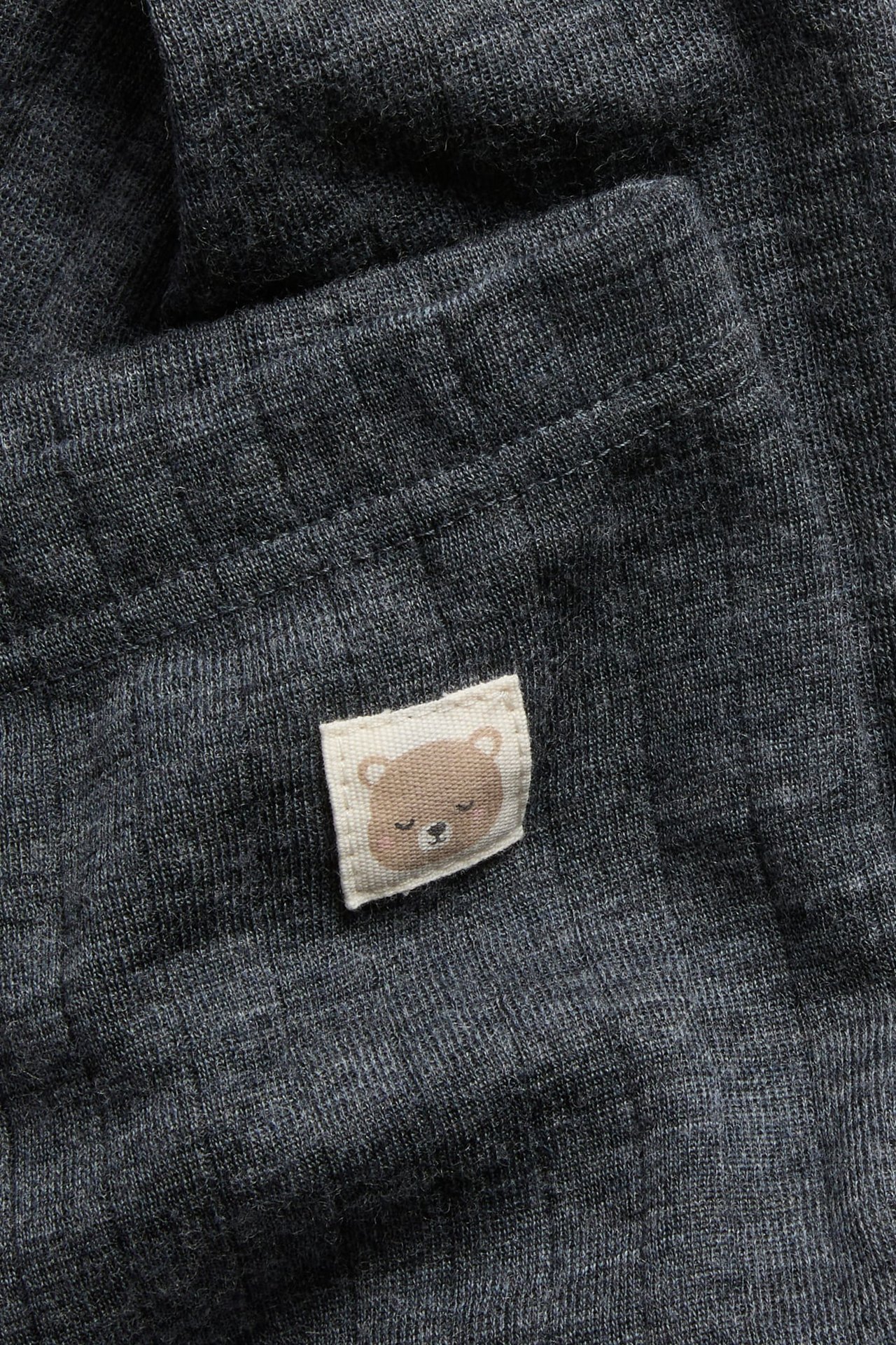 Närbild av mörkgrått stickat tyg med en liten sovande björn-etikett.
