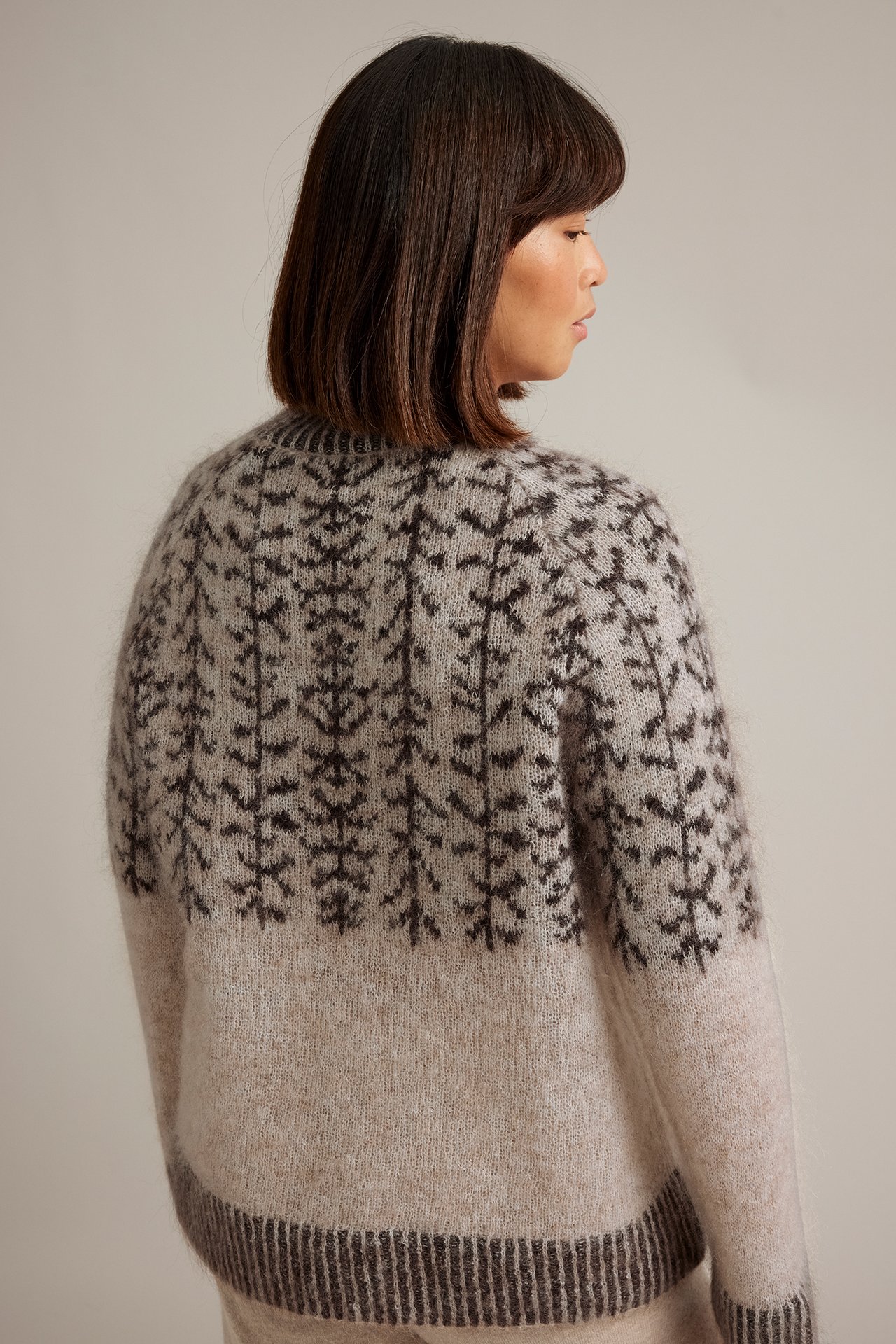 Naisen takaapäin, vaaleanbeige pörröinen Fair Isle -neule tummalla puukuviolla.