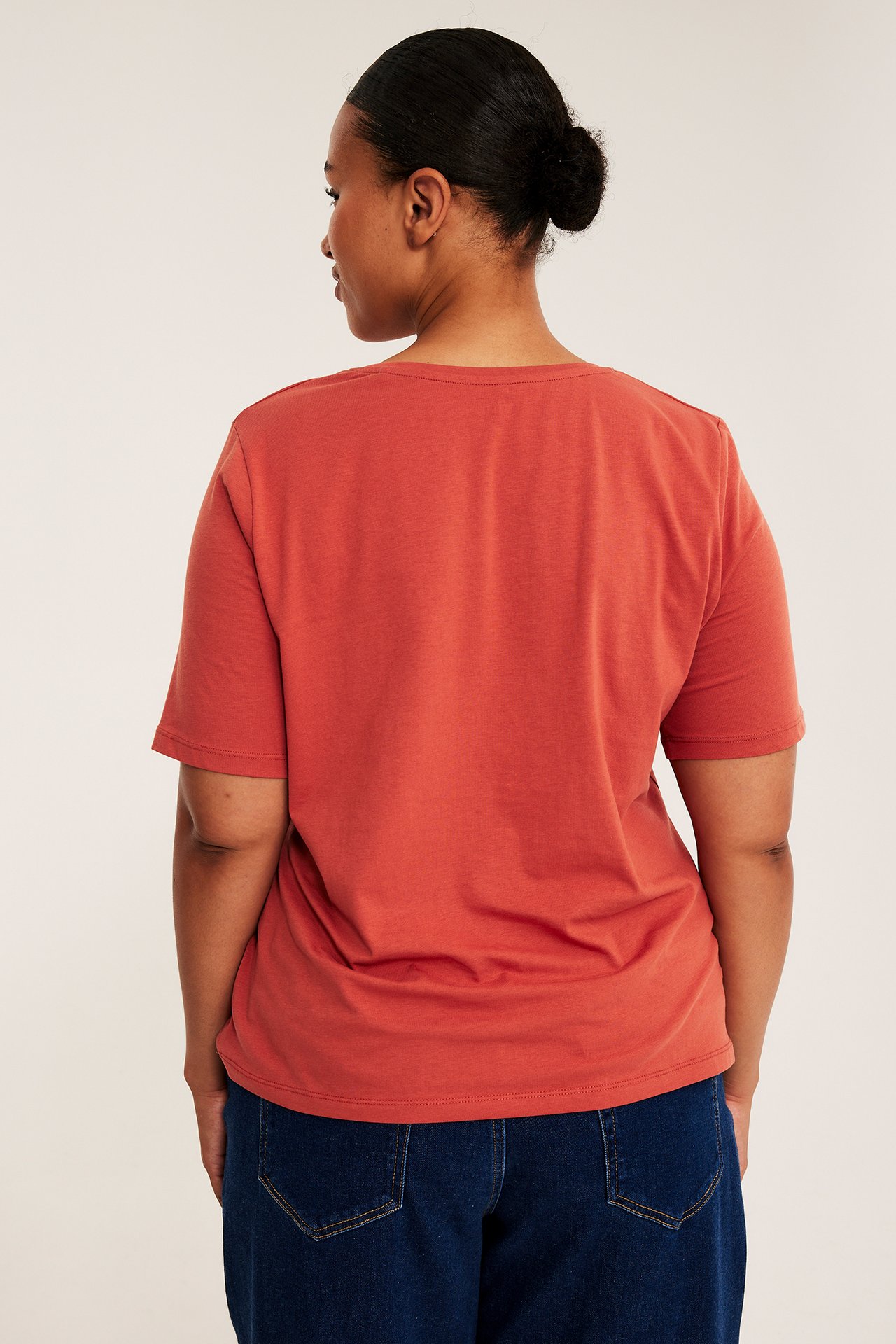 Ryggvy av kvinna i rostfärgad kortärmad t-shirt och mörkblå jeans.