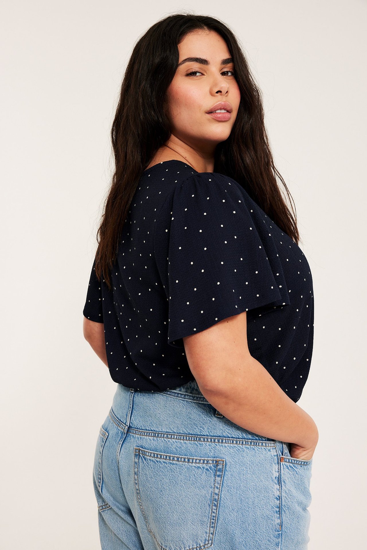 Side-bakfra av en kvinne i en mørkblå prikkete kortermet topp og lyseblå jeans.