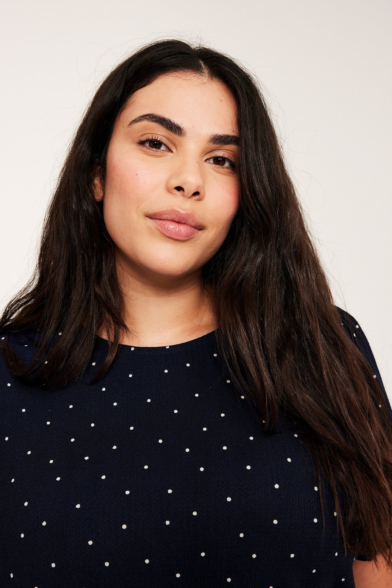 Nærbilde forfra av en kvinne i en mørk blå prikkete kortermet topp.