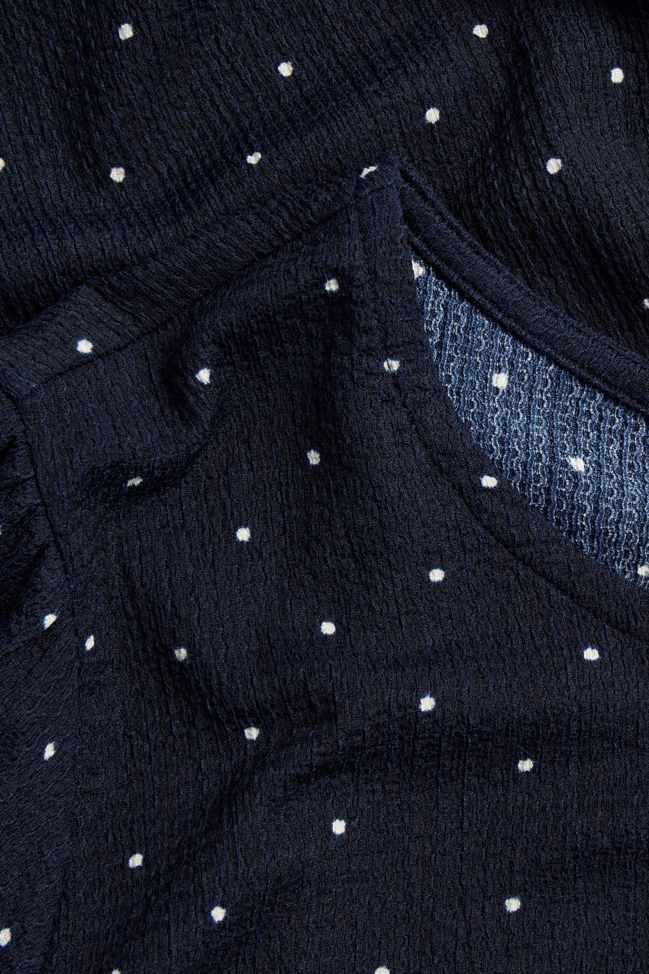 Nærbilde av en mørkeblå krøllete prikkete topp med hvite prikker og V-hals.